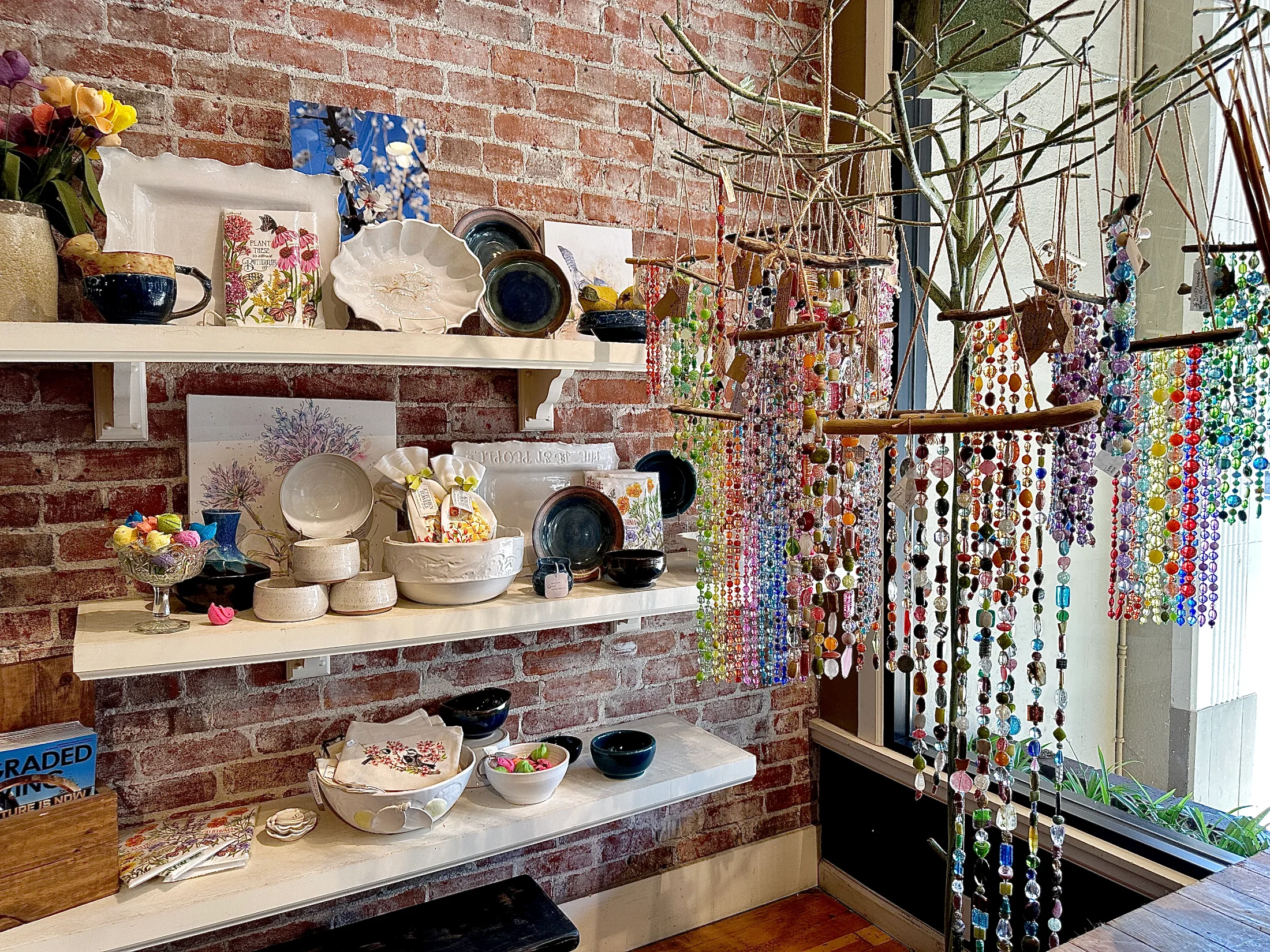 Interior shelves of Made in Chico showing handmade ceramics, pottery bowls, nature photography prints, and a colorful beaded curtain near the window