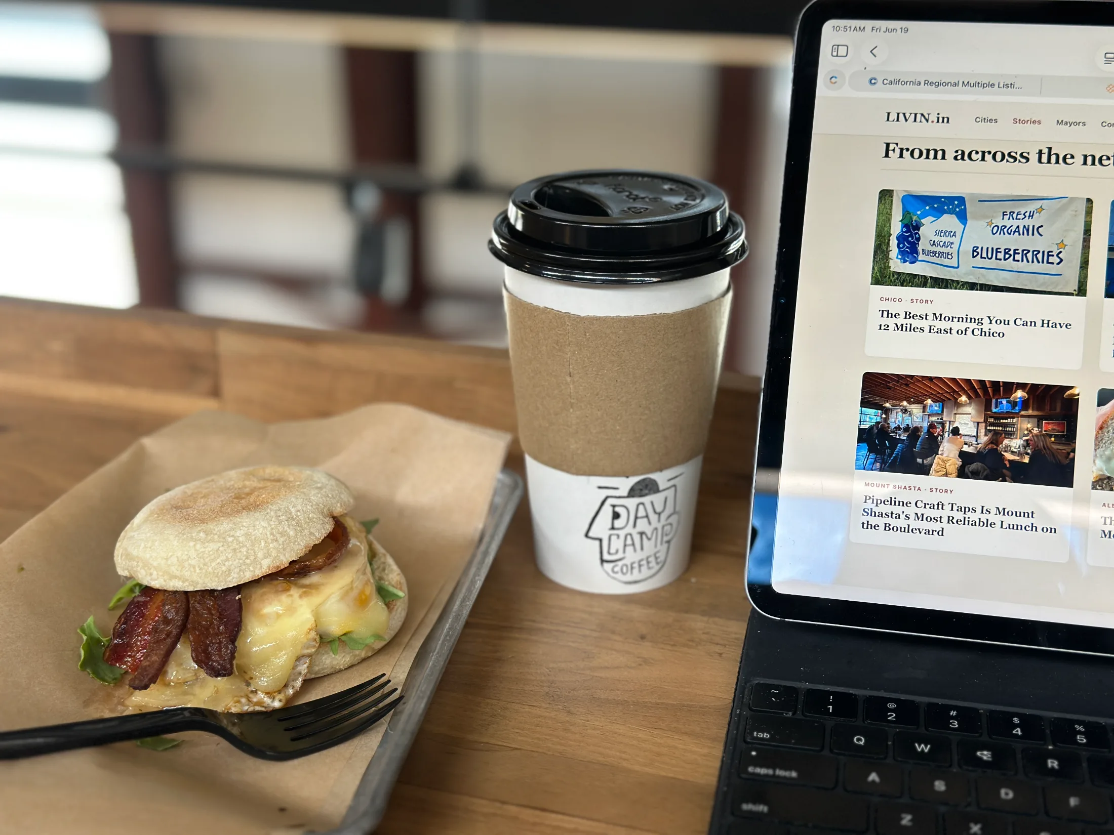 Breakfast sandwich on an English muffin with bacon and melted cheese next to a Daycamp Coffee cup on the upstairs work bar