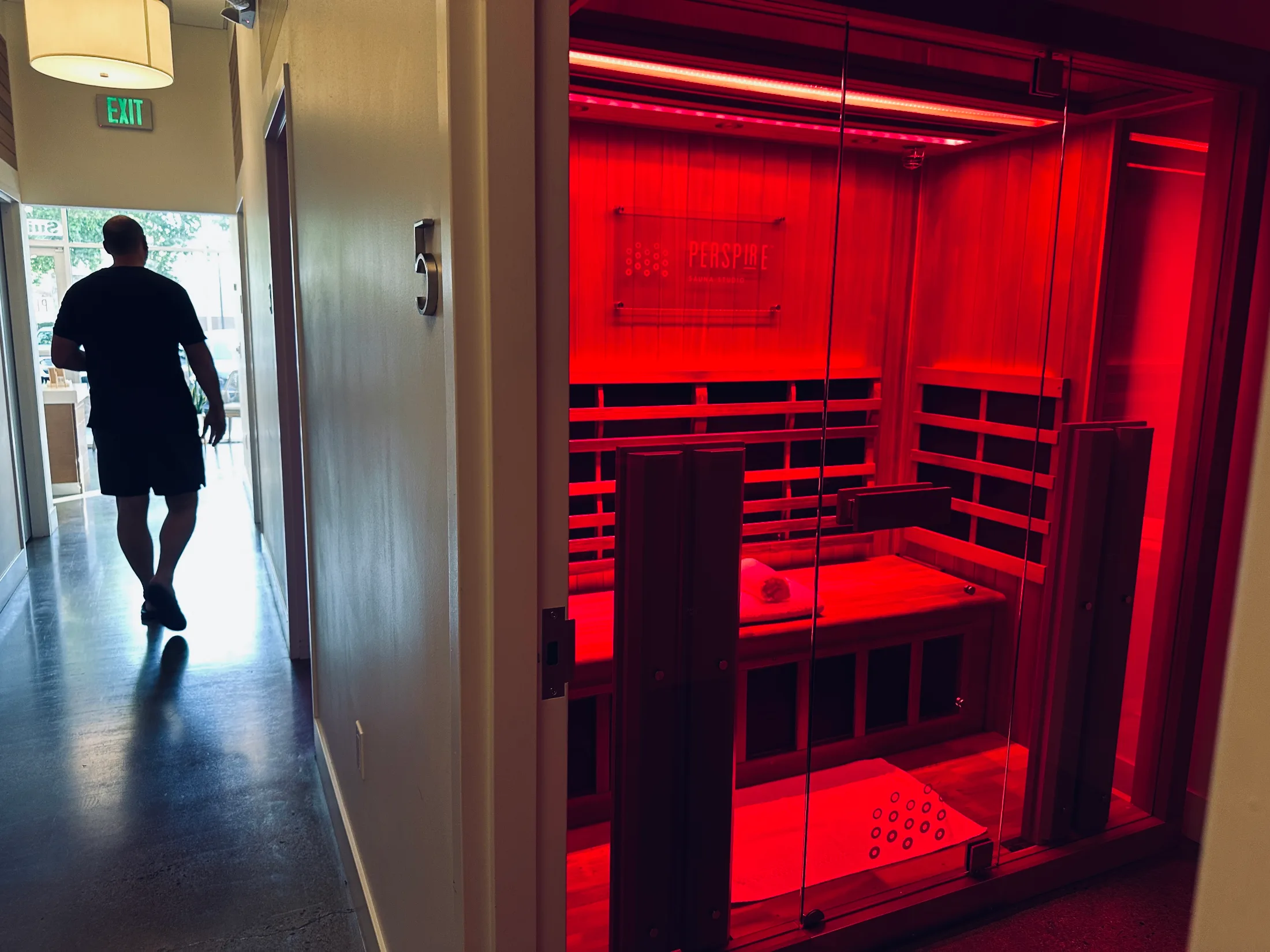 Man walking down the hallway past a glowing red infrared sauna suite at Perspire Sauna Studio
