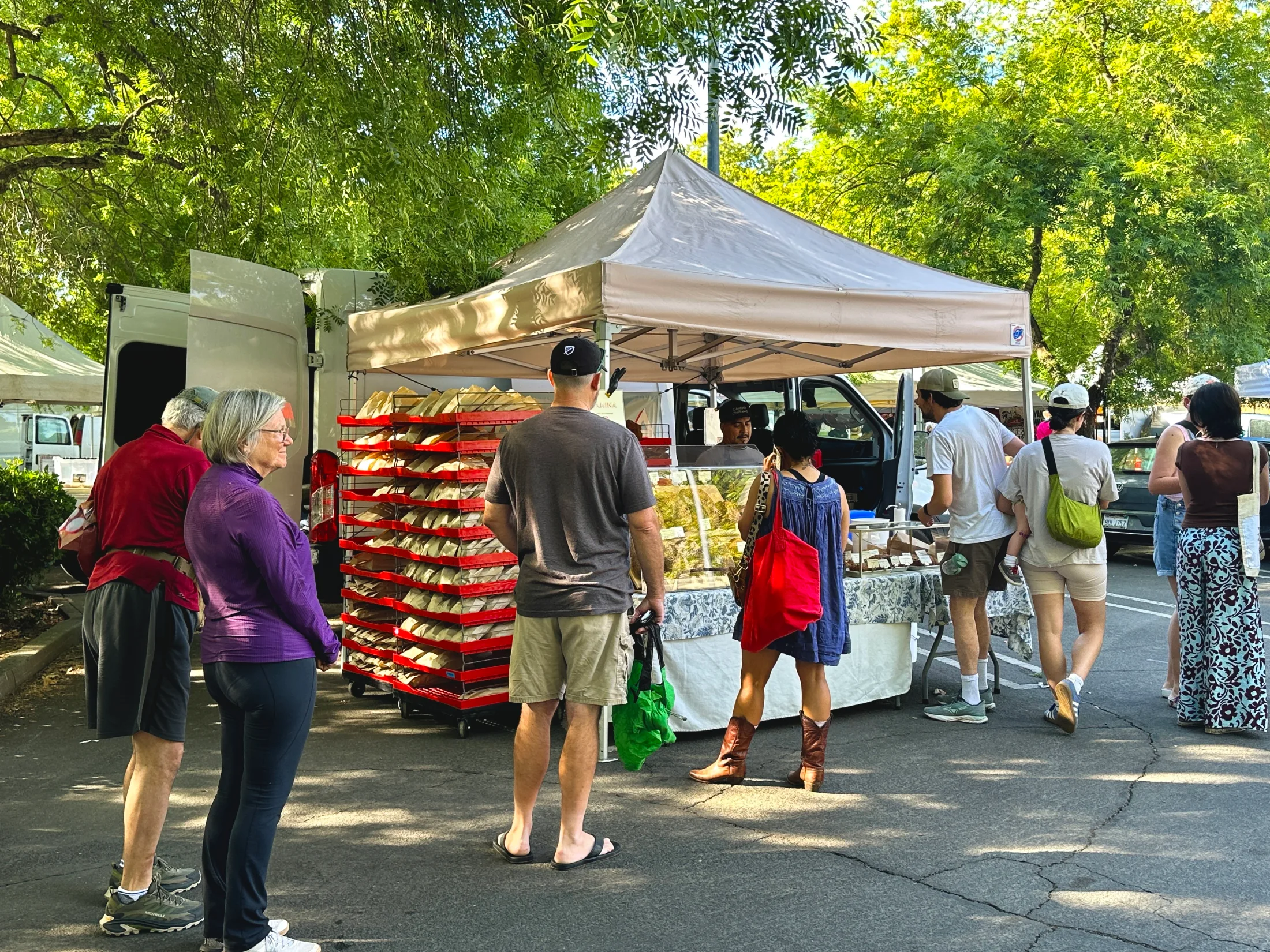 Shoppers lined up at a bread vendor stall stacked with fresh loaves at the farmers market