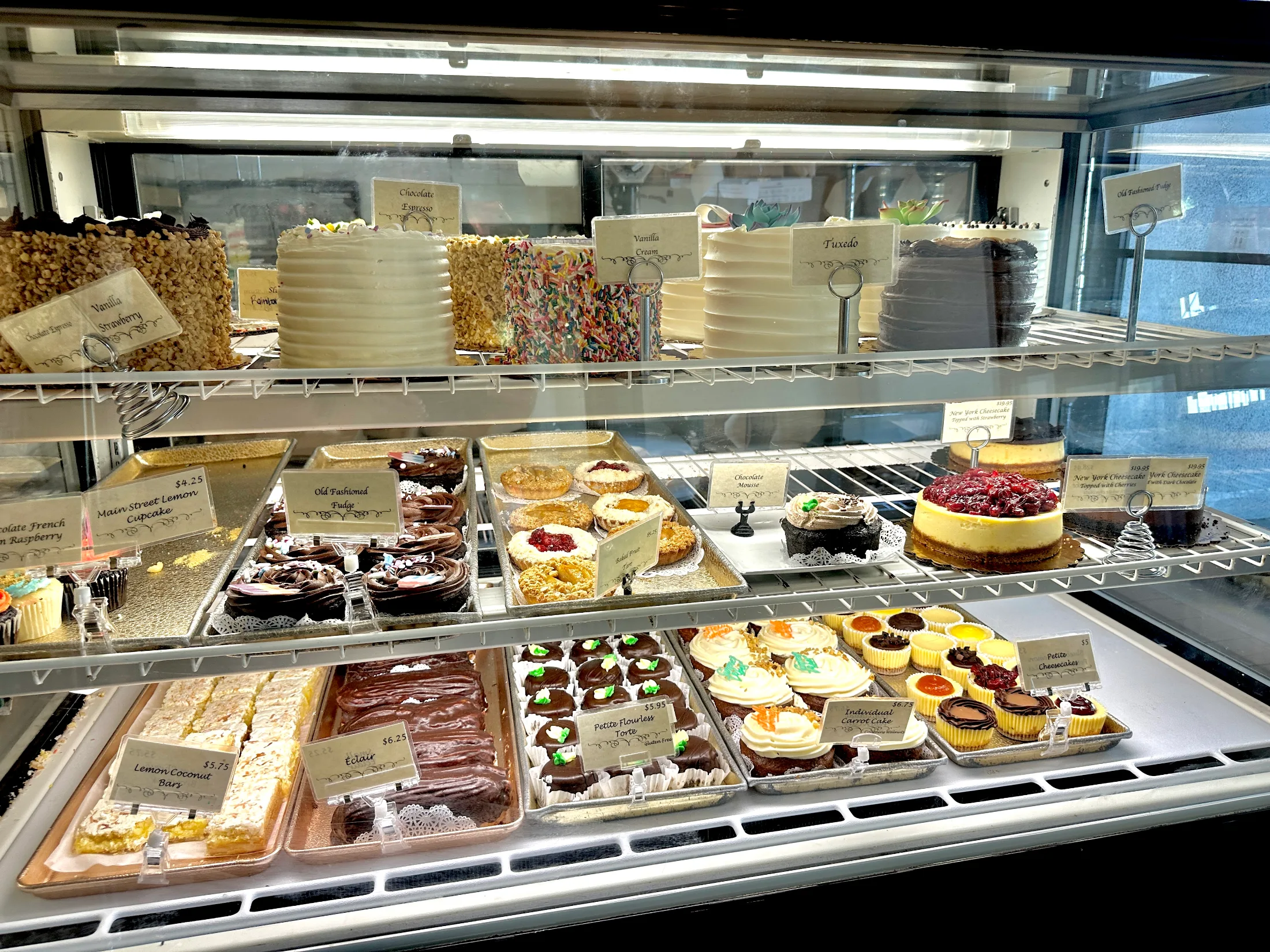Full display case at Upper Crust showing whole cakes on the top shelf and pastries, éclairs, and lemon bars below