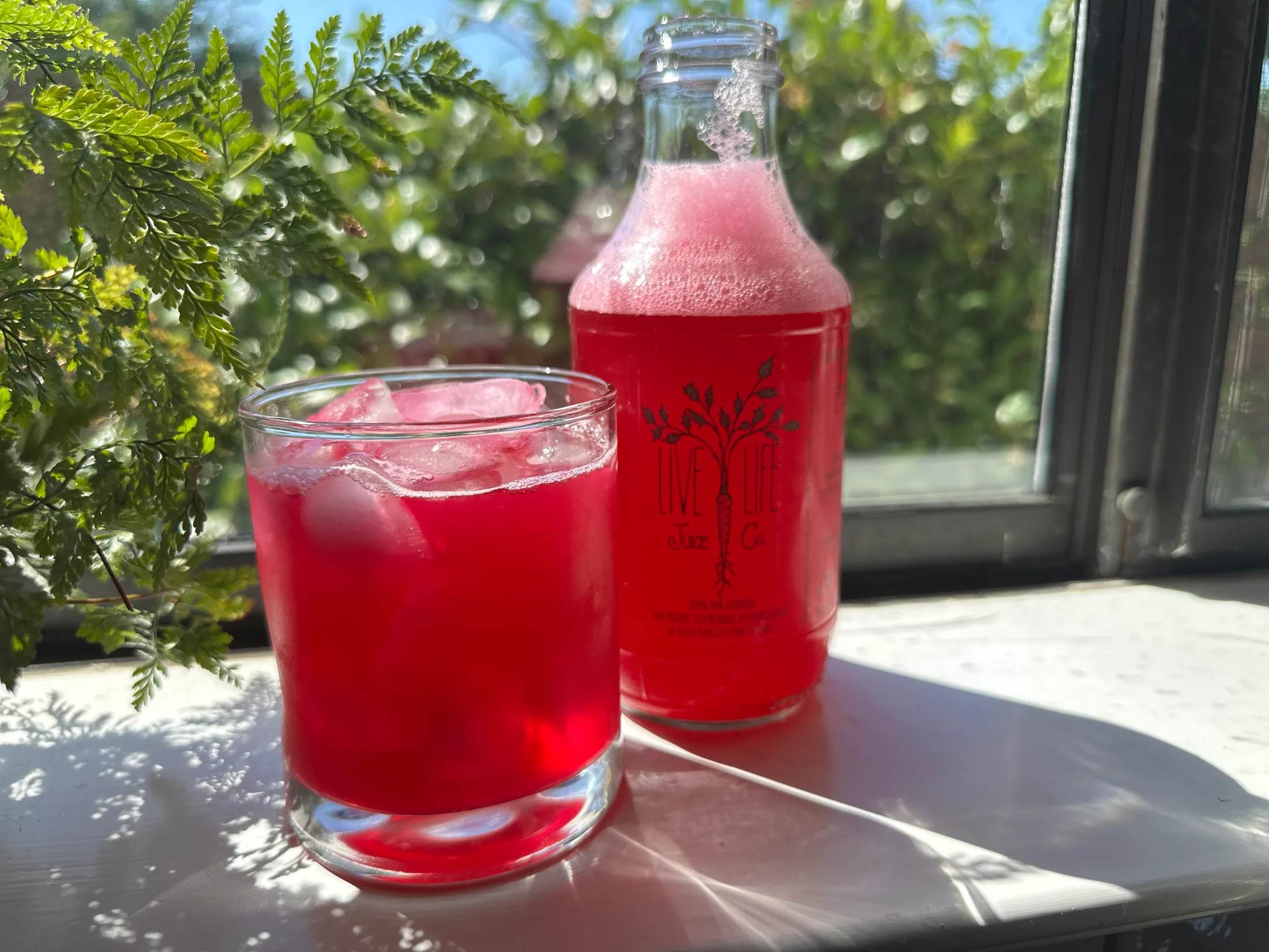 A bright red Live Life Juice Co. cold-pressed juice poured over ice next to the branded glass bottle