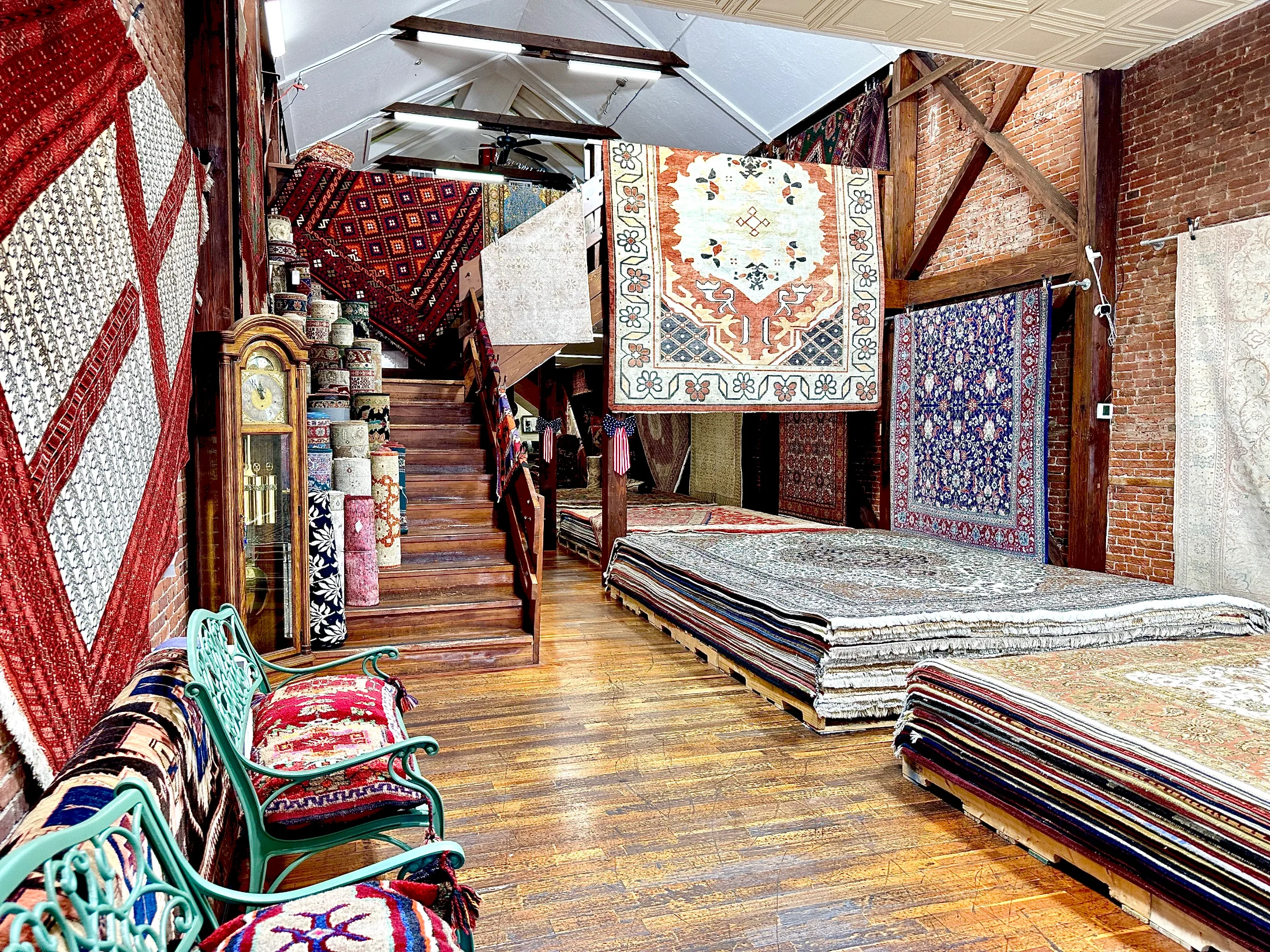 Interior of Pasha Hand Crafted Rugs showing rugs hung on brick walls and stacked on platforms