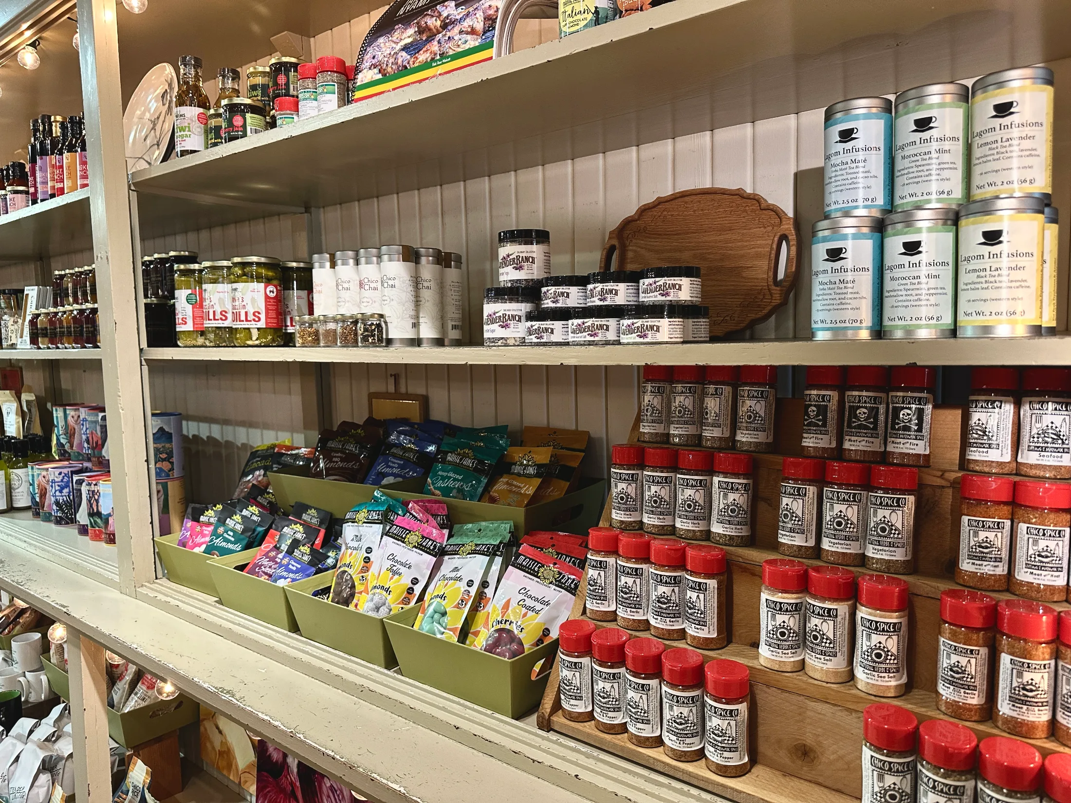 Shelves of local food products inside Made in Chico including Chico Spice Co. rubs, Lagom Infusions teas, Chico Chai, and chocolate-covered almonds