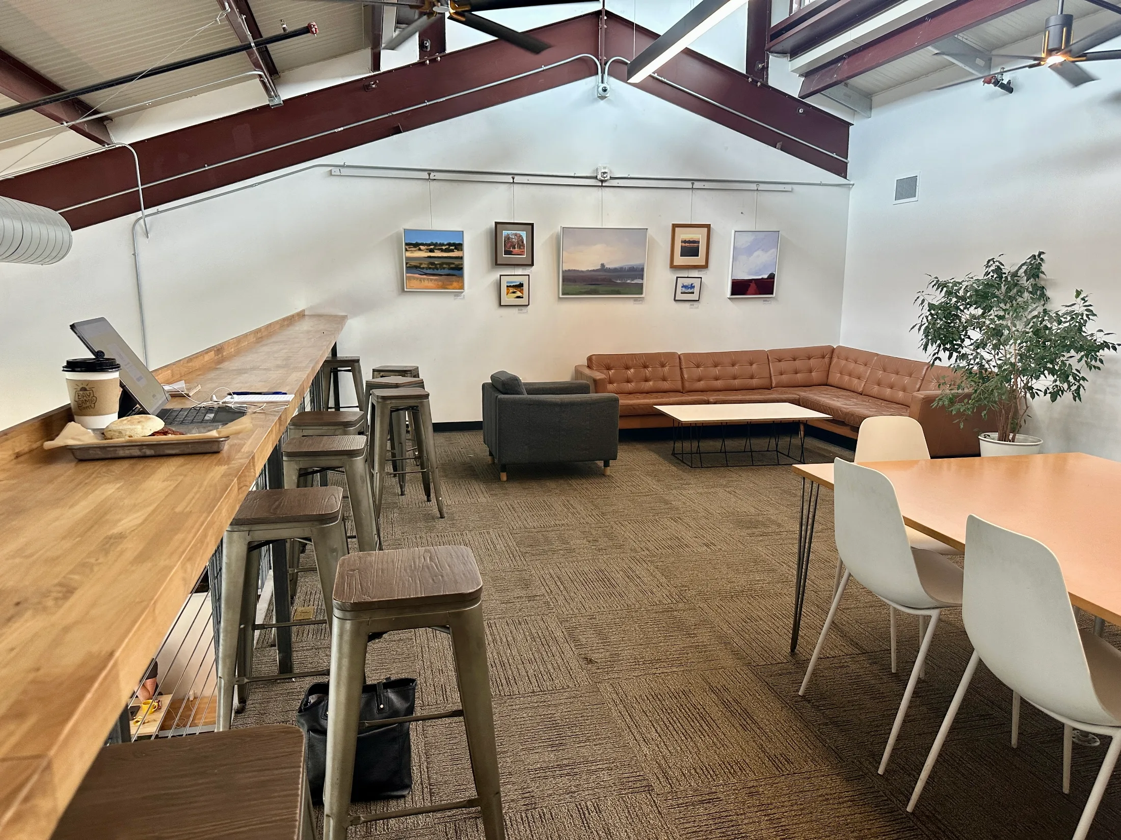 Upstairs mezzanine at Daycamp Coffee with a wood bar counter, bar stools, leather sectional couch, and local artwork on the walls