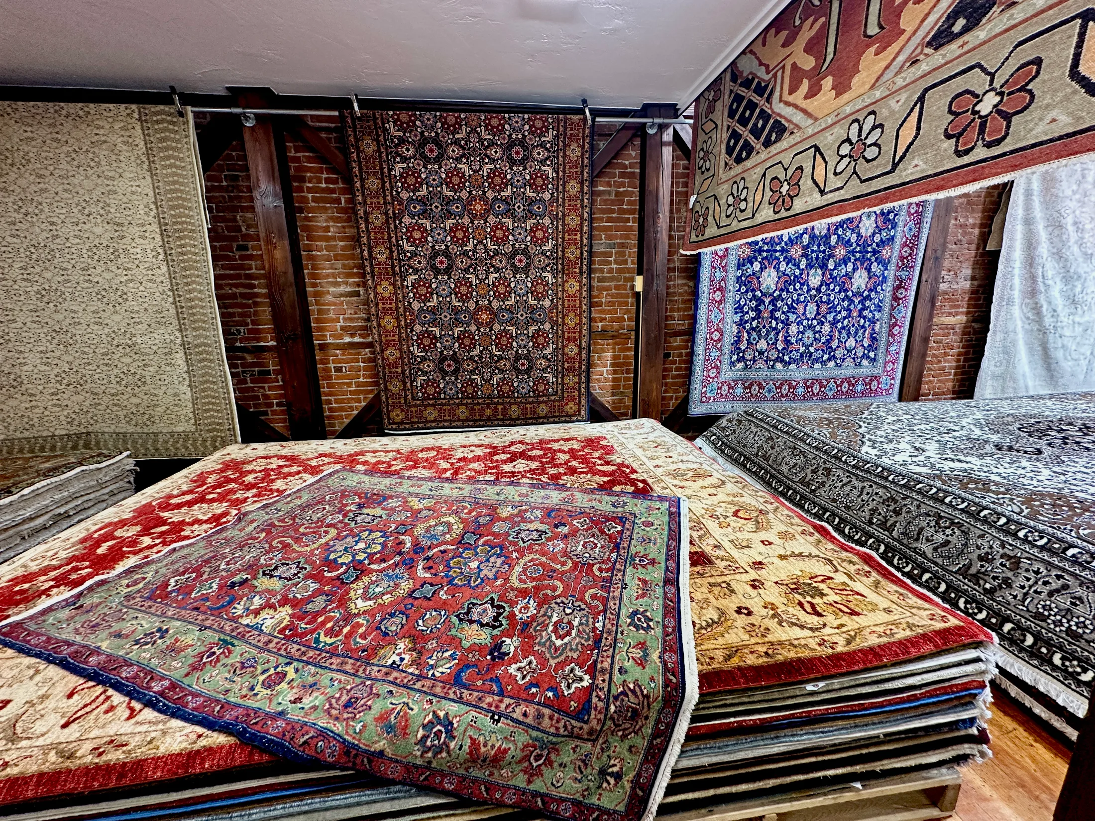 Stacks and rows of hand-knotted rugs in vibrant reds, blues, and neutrals inside Pasha Hand Crafted Rugs