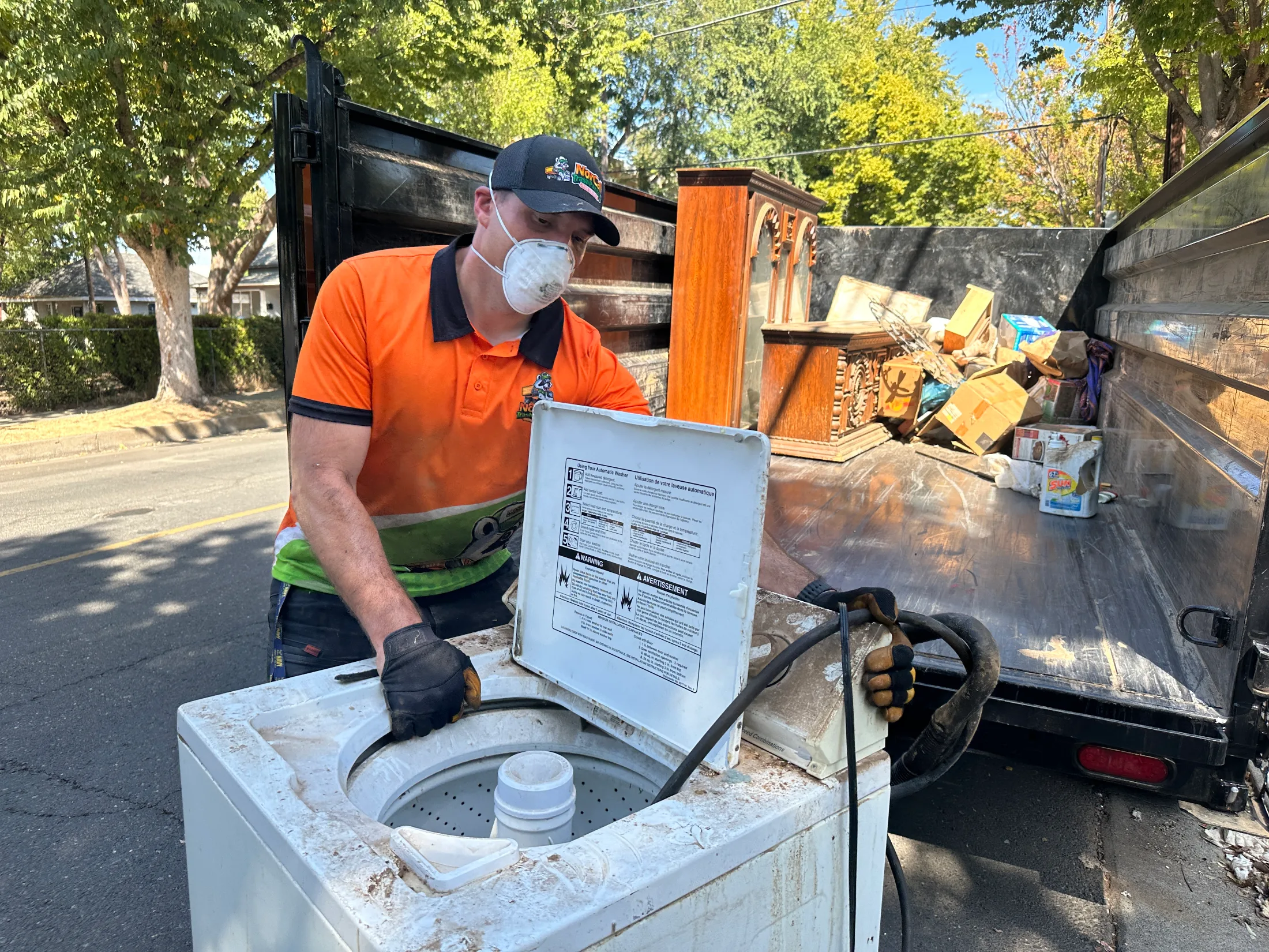 NorCal Trash Pandas crew member loading a washing machine and furniture into a junk removal trailer on a Chico street