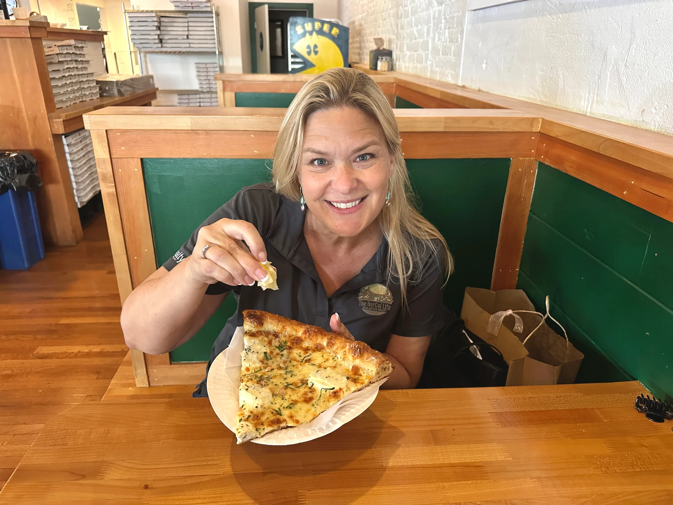 Woman smiling in a green booth at Bodega Slice Shop, squeezing a lemon wedge over a large white-pie slice