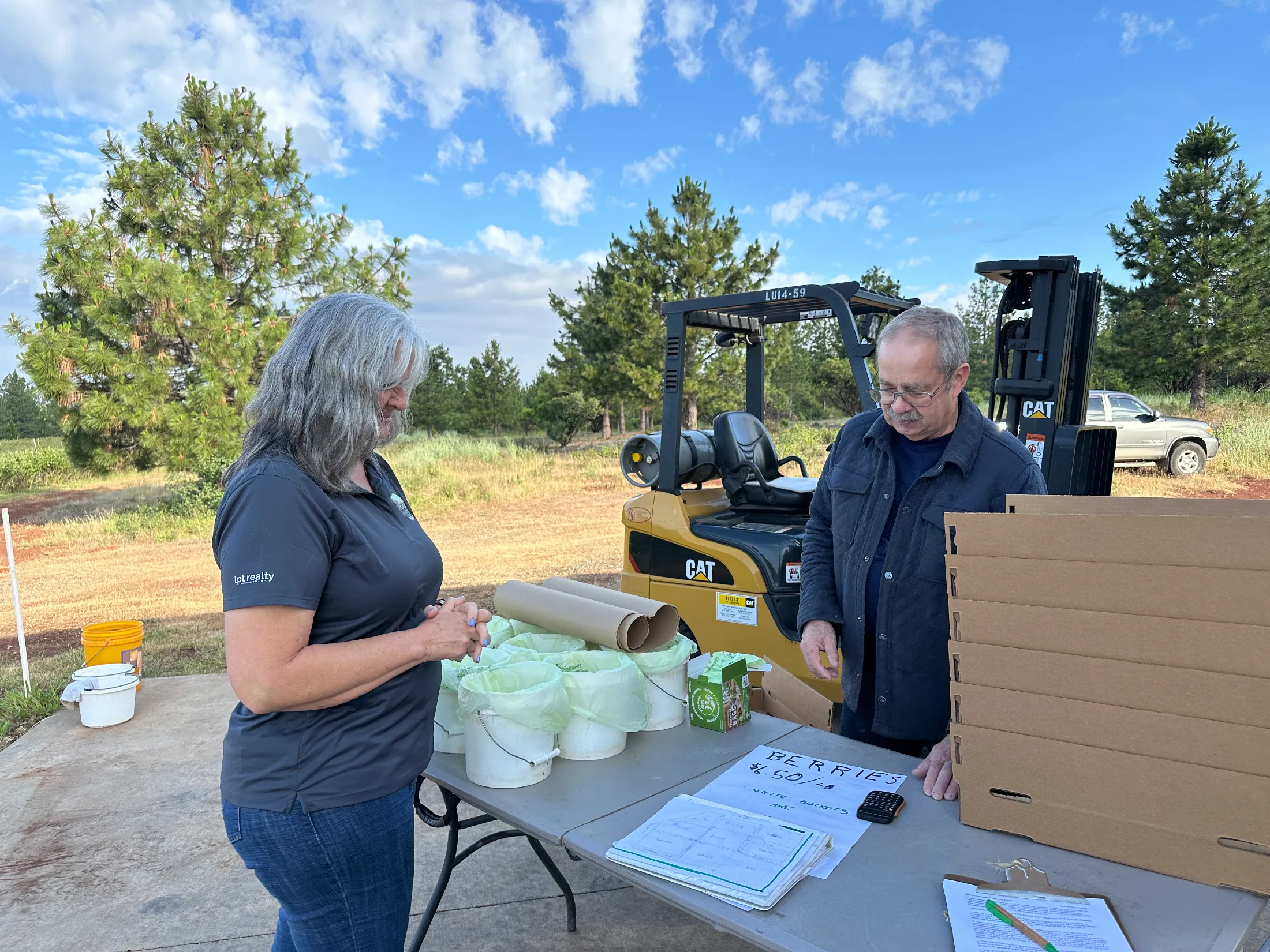 Woman checking in at the farm's outdoor weigh station, sign reading Berries $6.50/lb