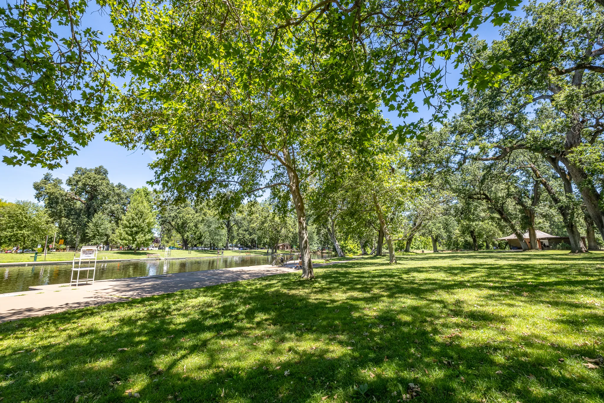 Shaded lawn and swimming hole at One Mile Recreation Area with a lifeguard stand visible along the water's edge