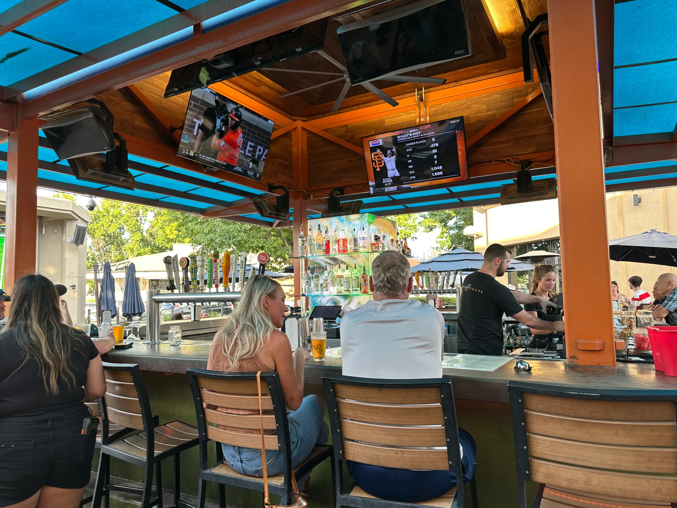 Guests seated at the outdoor bar at Pour House with sports on screens and warm evening light
