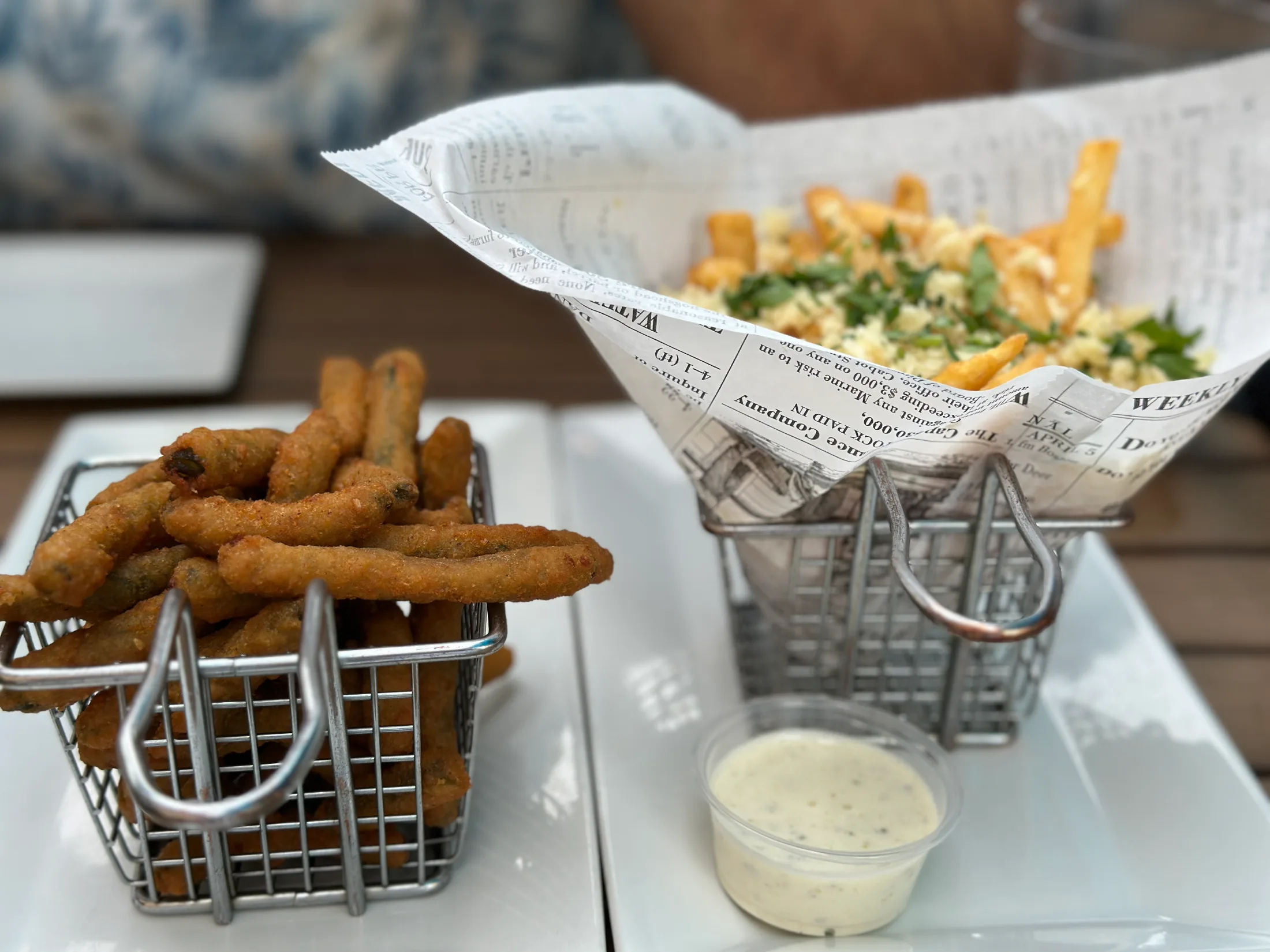 Deep fried green beans in a wire basket alongside loaded fries, served on a white plate at Pour House