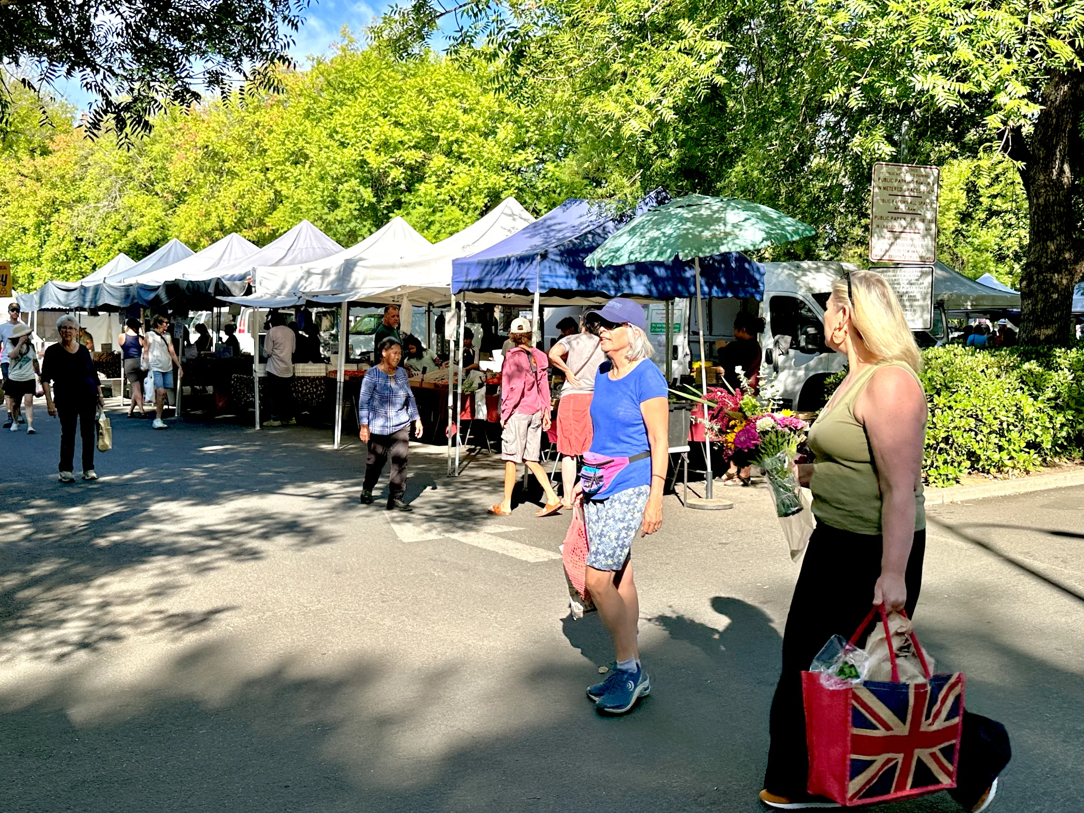 Shoppers walking through the Chico Certified Farmers Market under shady trees on a sunny morning