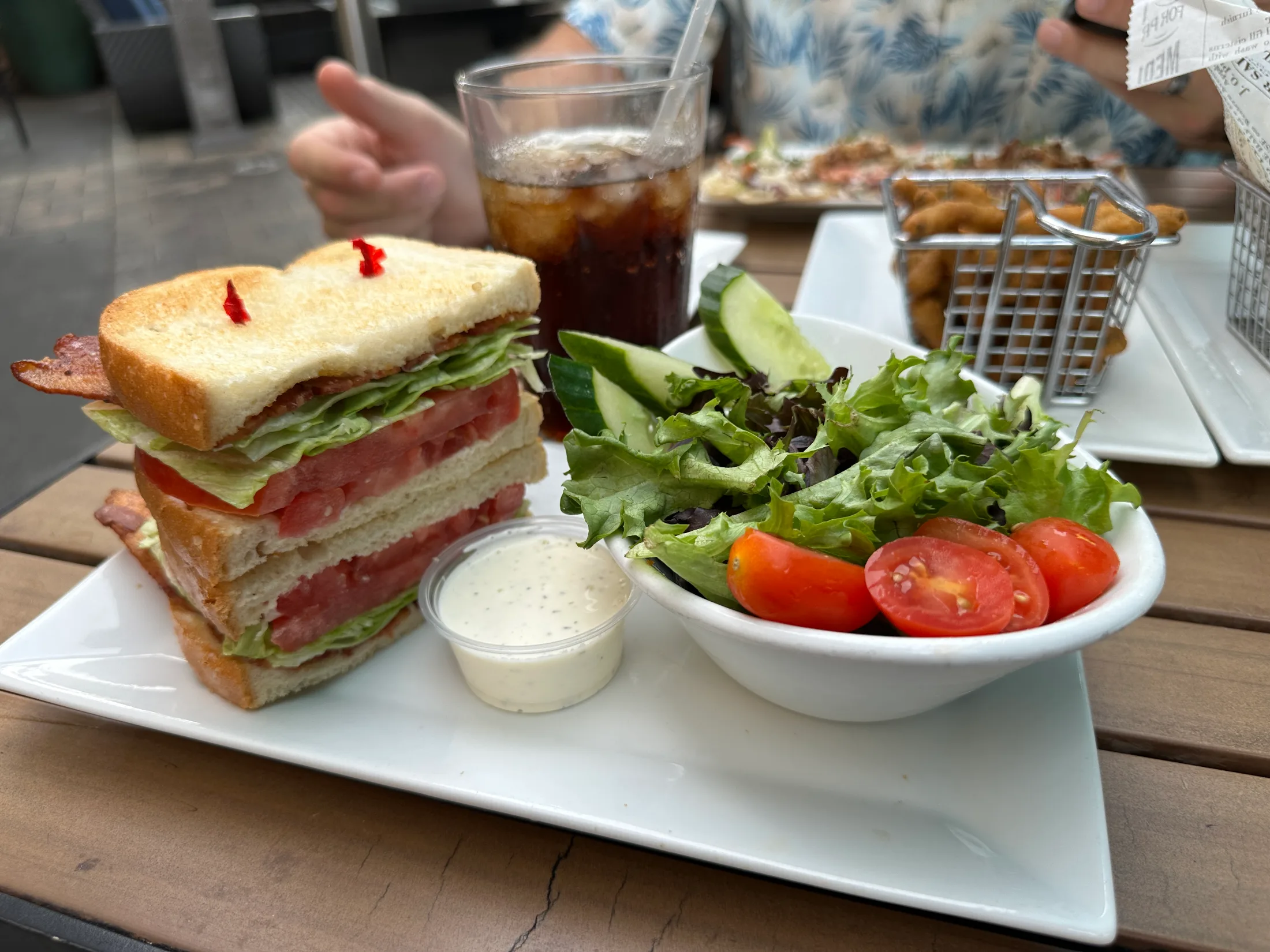 BLT sandwich stacked tall with bacon, lettuce, and tomato on toasted sourdough bread, served with a side salad at Pour House