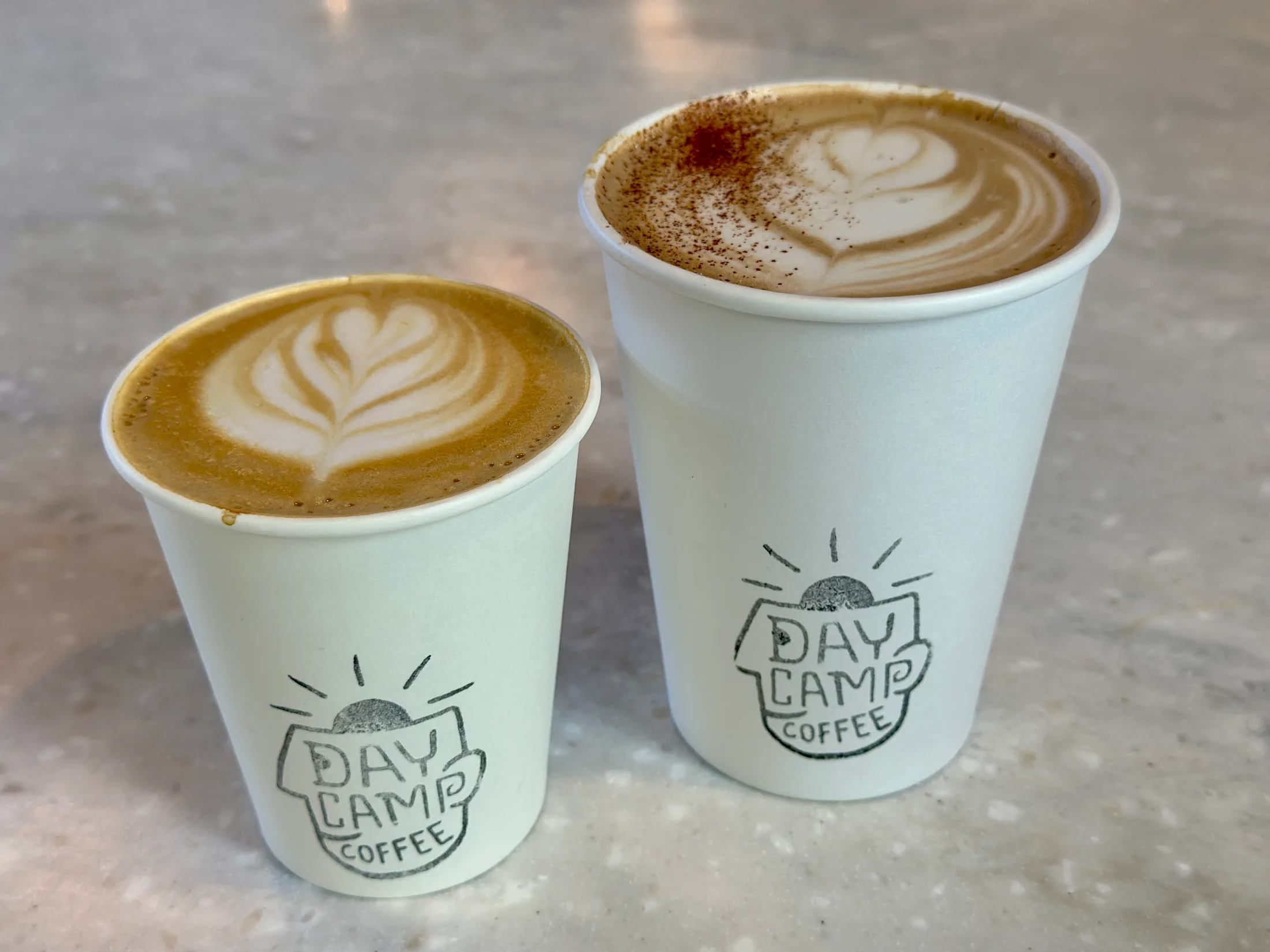 Two Daycamp Coffee lattes with latte art in branded paper cups