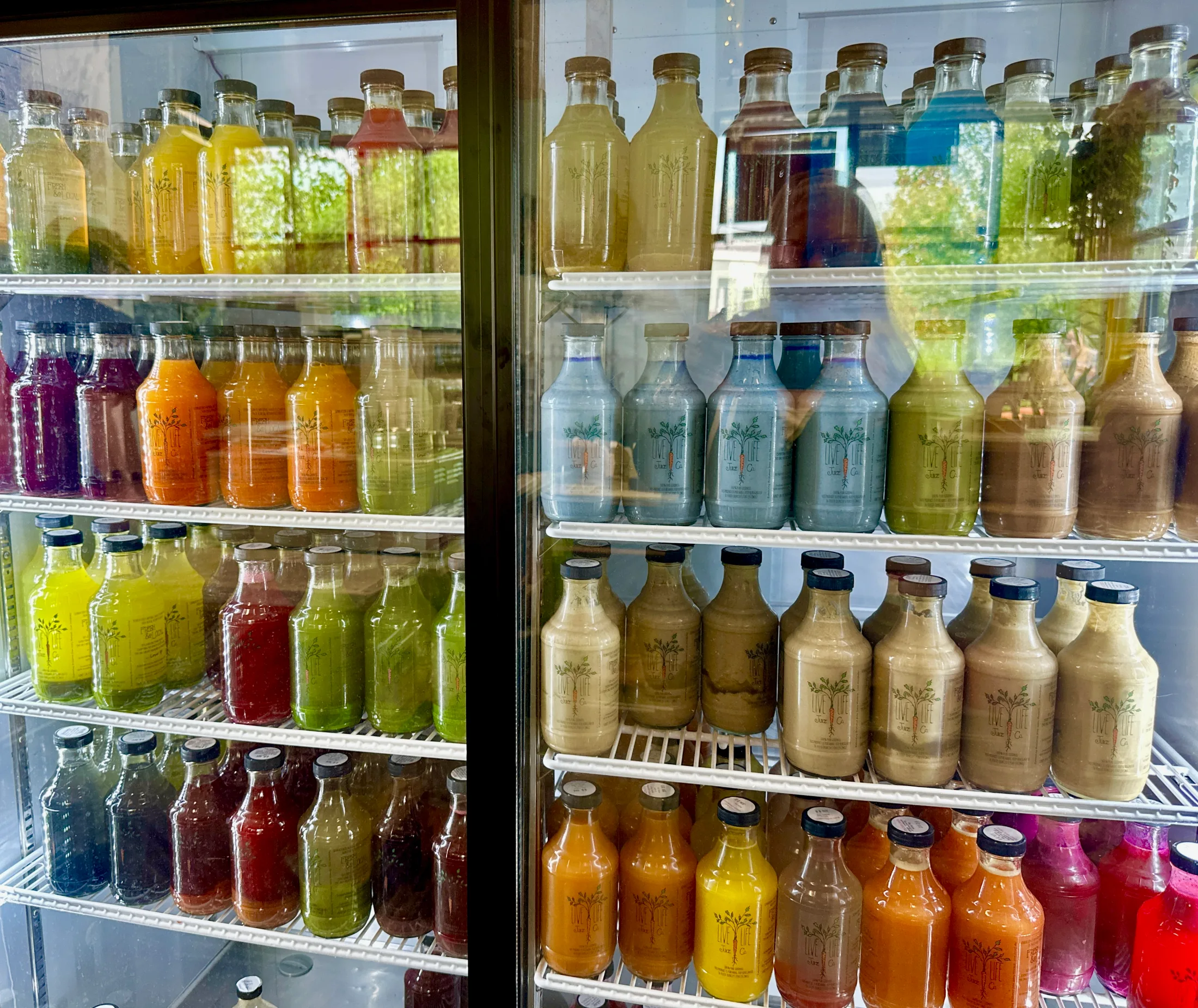 Glass-door refrigerator case packed with rows of colorful cold-pressed juice bottles in every shade from green to red to blue
