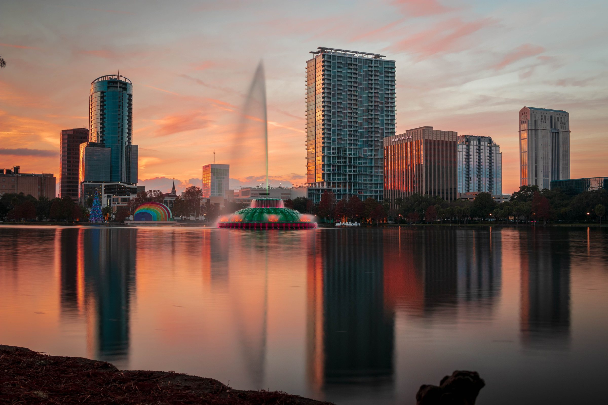 The Lake Eola fountain at sunset with downtown Orlando towers reflected in the lake