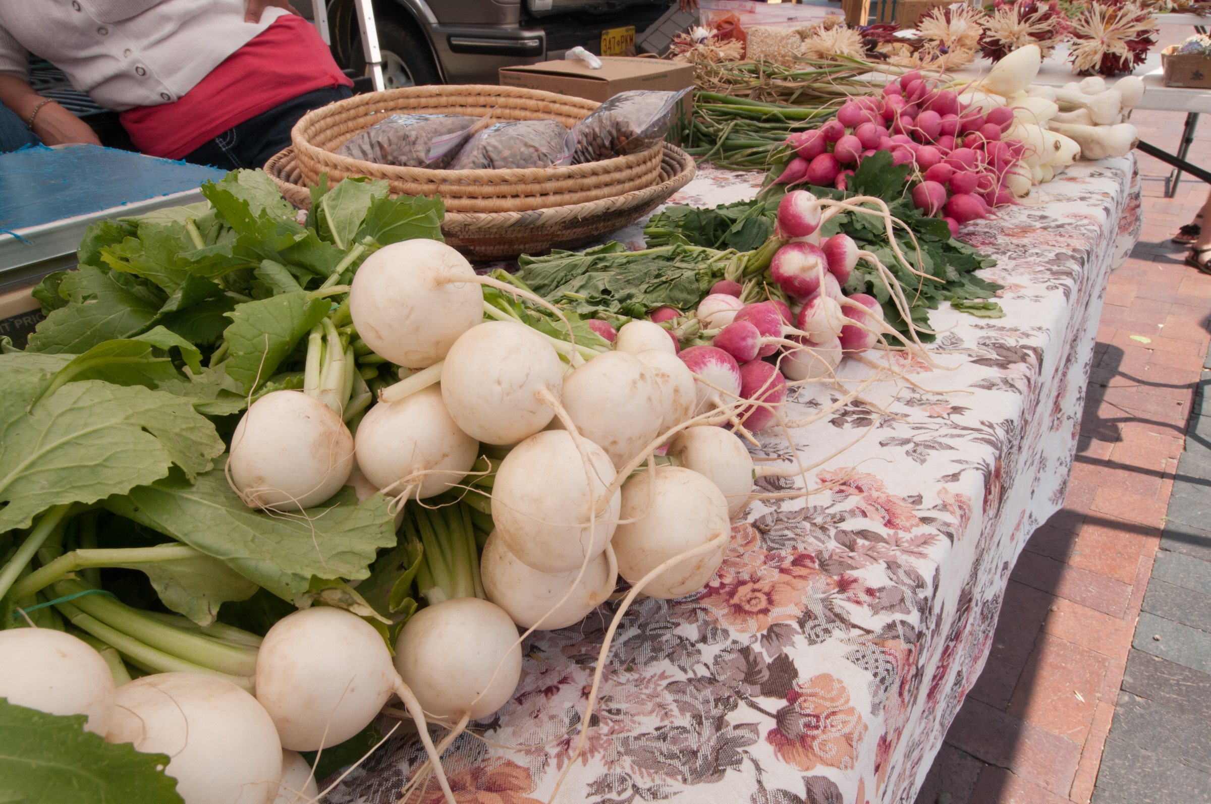 Bunches of white turnips, radishes and greens on a flowered tablecloth at the Santa Fe Farmers' Market