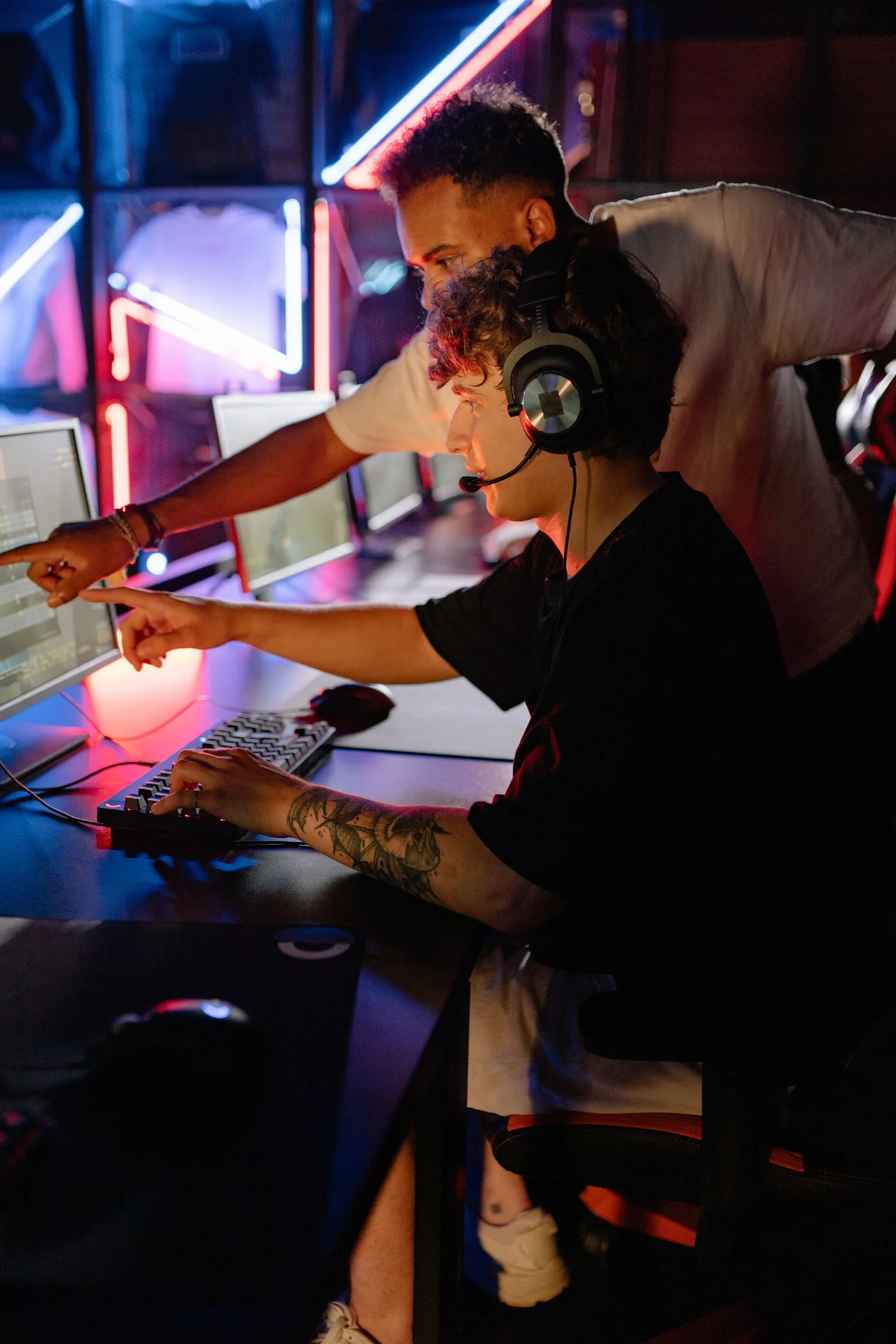 Two tech workers collaborating at a computer setup under neon lighting