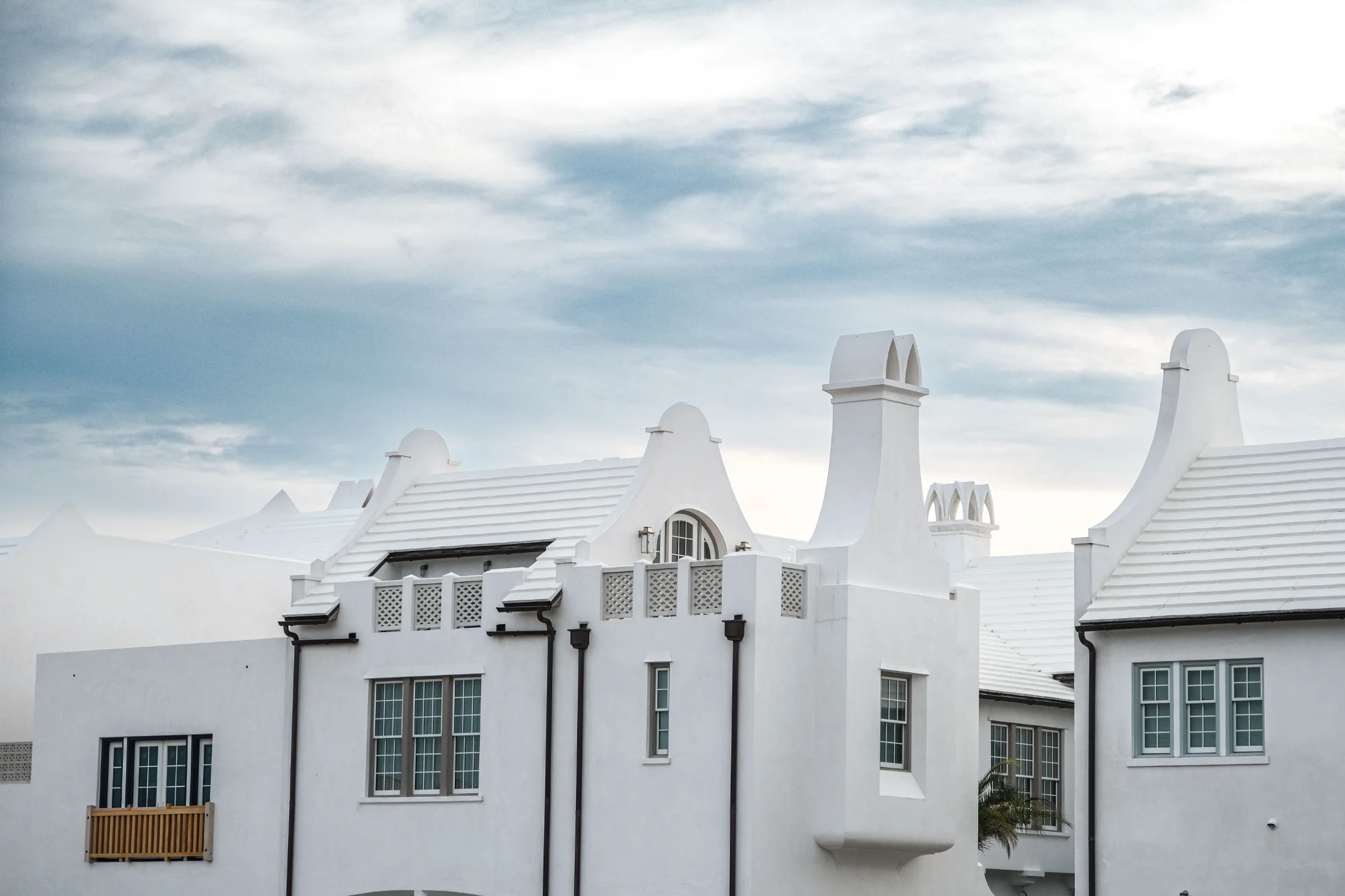 Alys Beach white stucco buildings with ornate parapet details, dark iron lanterns, and green-trimmed windows under an overcast sky