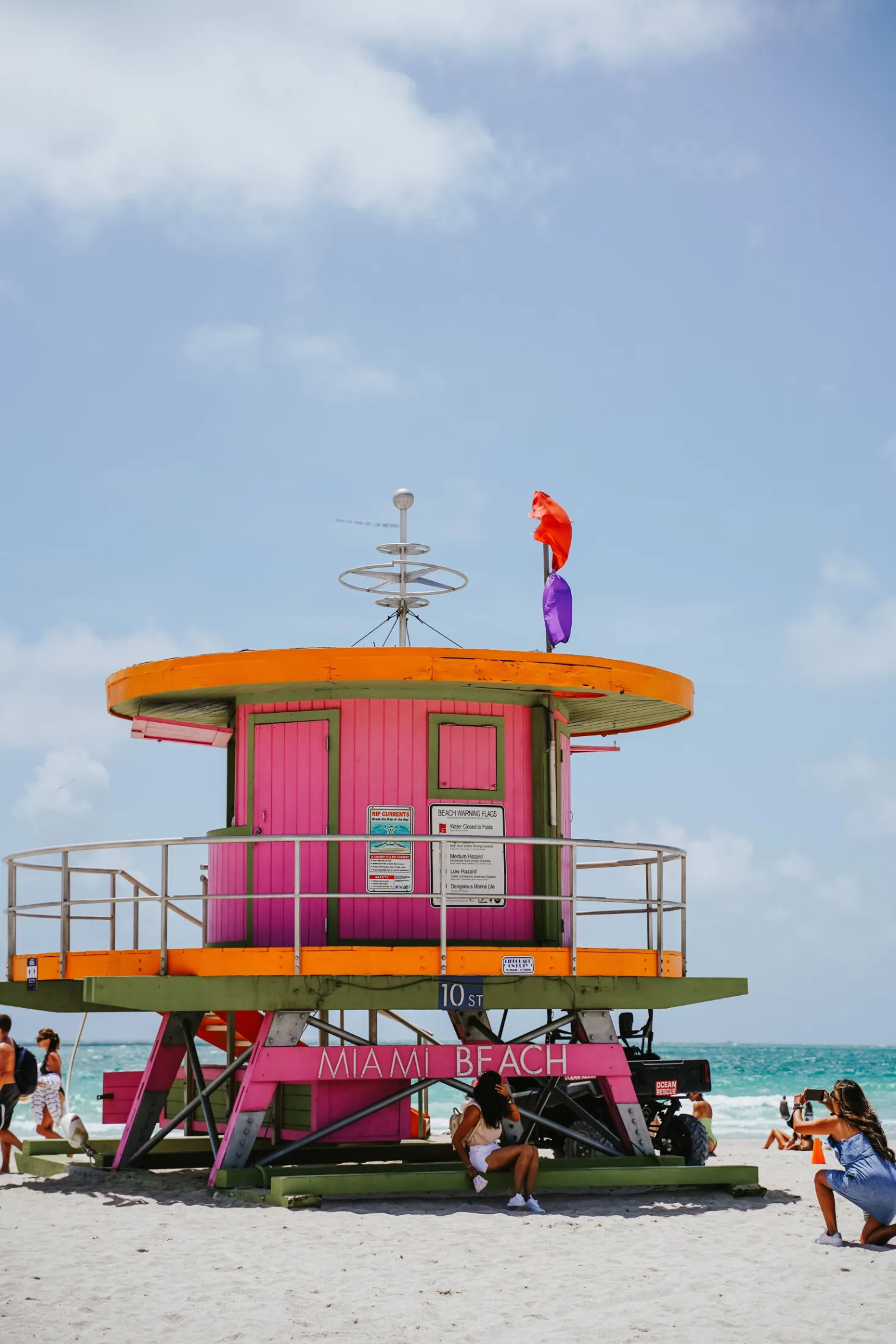 The iconic pink and orange round Miami Beach lifeguard station at 10th Street with people posing for photos and the ocean behind