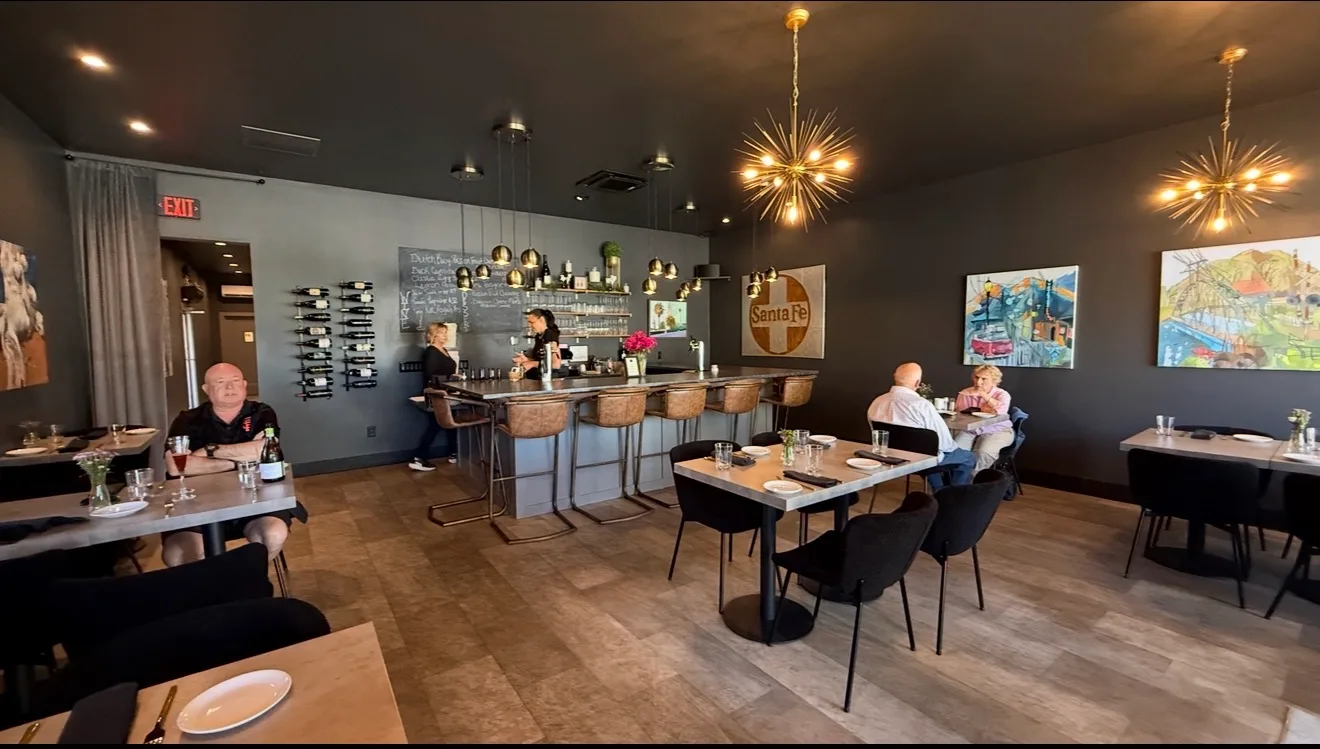Inside Baldovinos Wine Bar — warm gold Sputnik chandeliers, a wine-lined bar, local artwork on charcoal walls, and guests dining at stone-topped tables