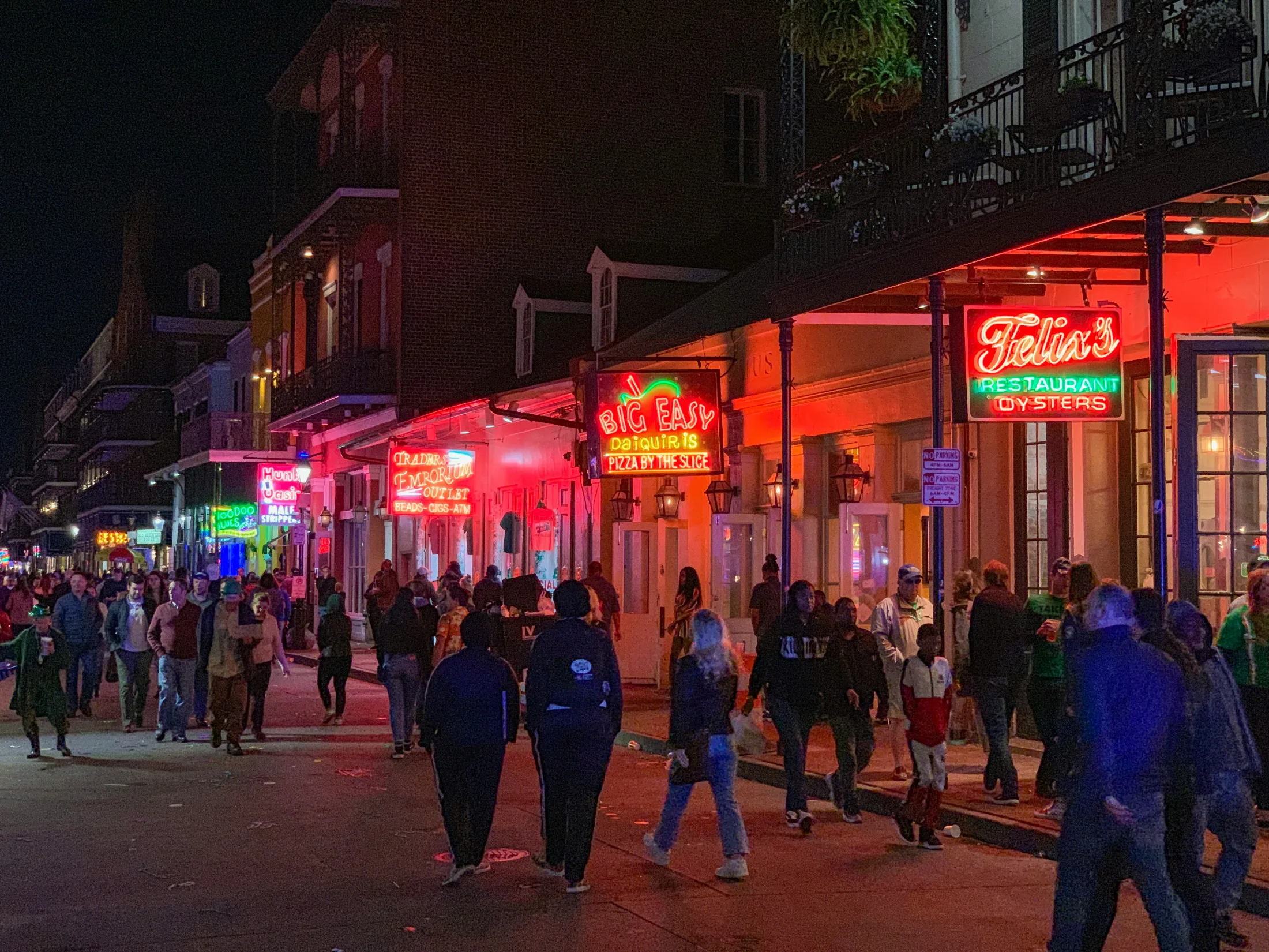 Pedestrians walking a neon-lit New Orleans street after dark, theatre and bar signs glowing overhead.