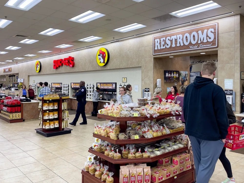 Busy Buc-ee's interior with shoppers, stacked baked goods, and the famous Buc-ee's beaver logo on the wall