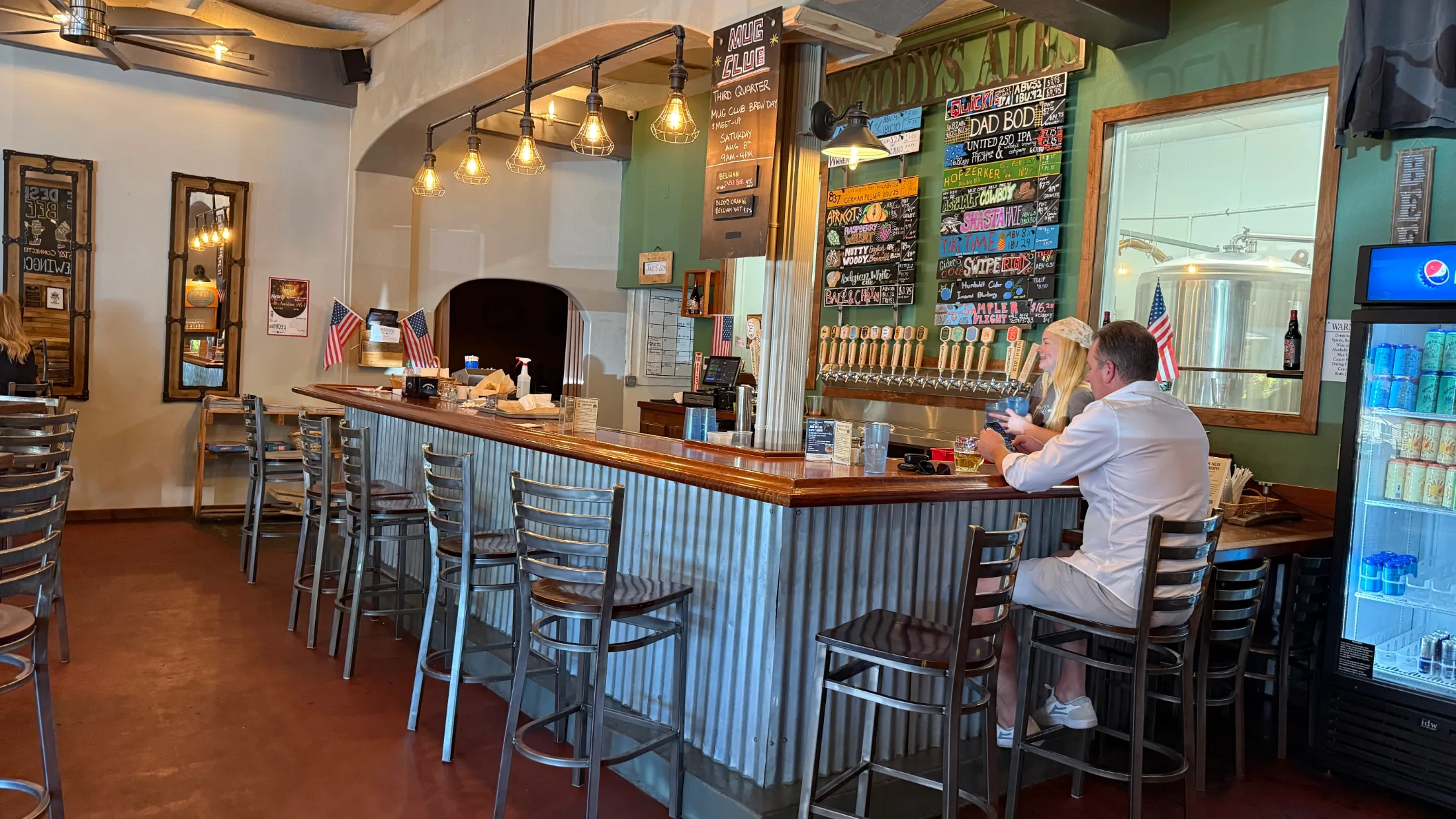 The interior bar at Woody's Brewing Company, with a long tap wall, Edison bulb pendant lights, and guests seated at the bar