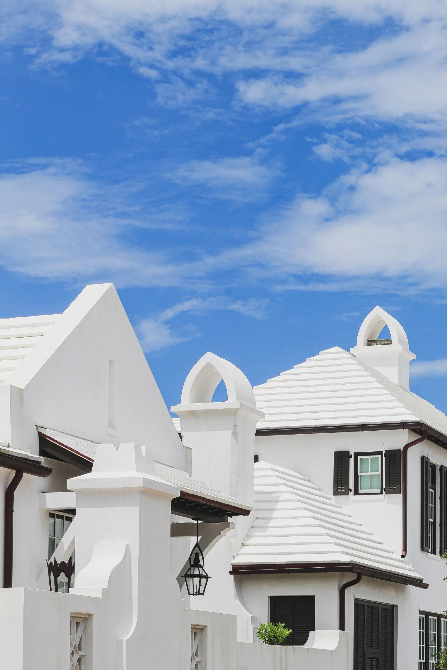 White stucco rooflines with gothic-arched cupolas and black shutters against a blue Florida sky in Alys Beach