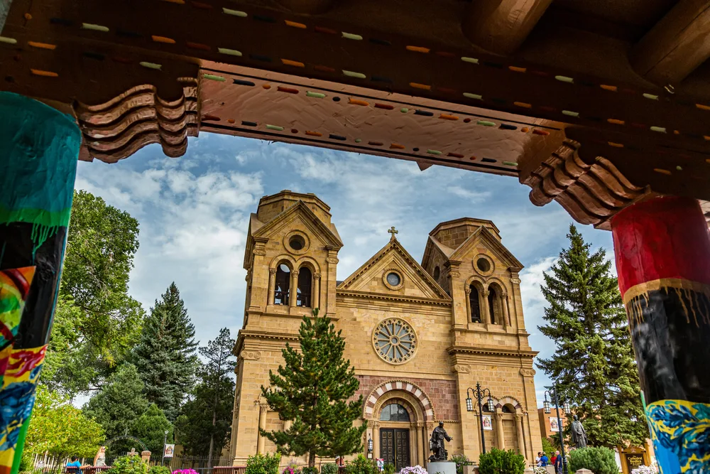 Cathedral Basilica of St. Francis of Assisi framed by hand-painted folk art portal columns under a dramatic cloudy sky