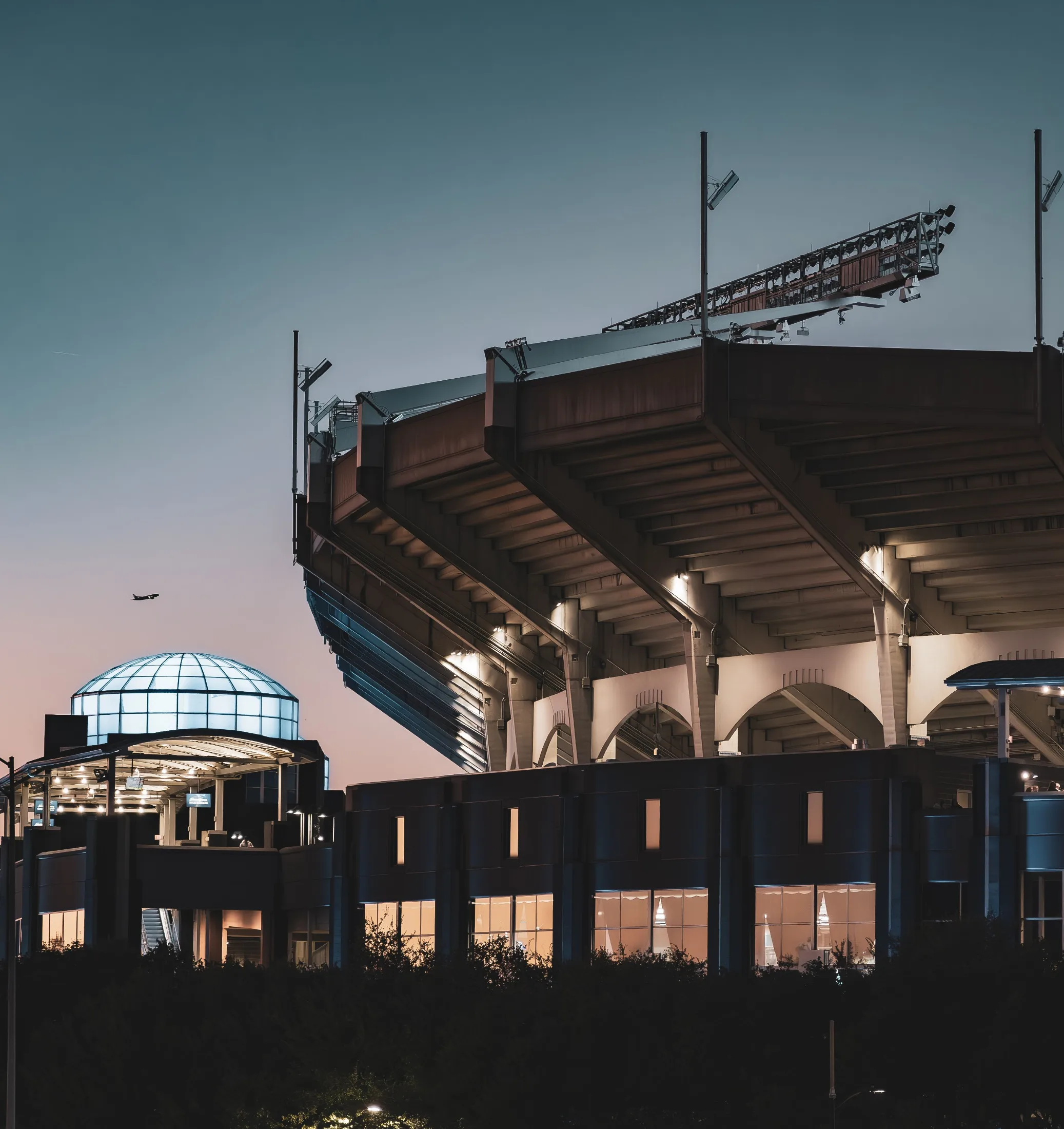 Bank of America Stadium lit at dusk, a plane visible in the distance over the Charlotte skyline