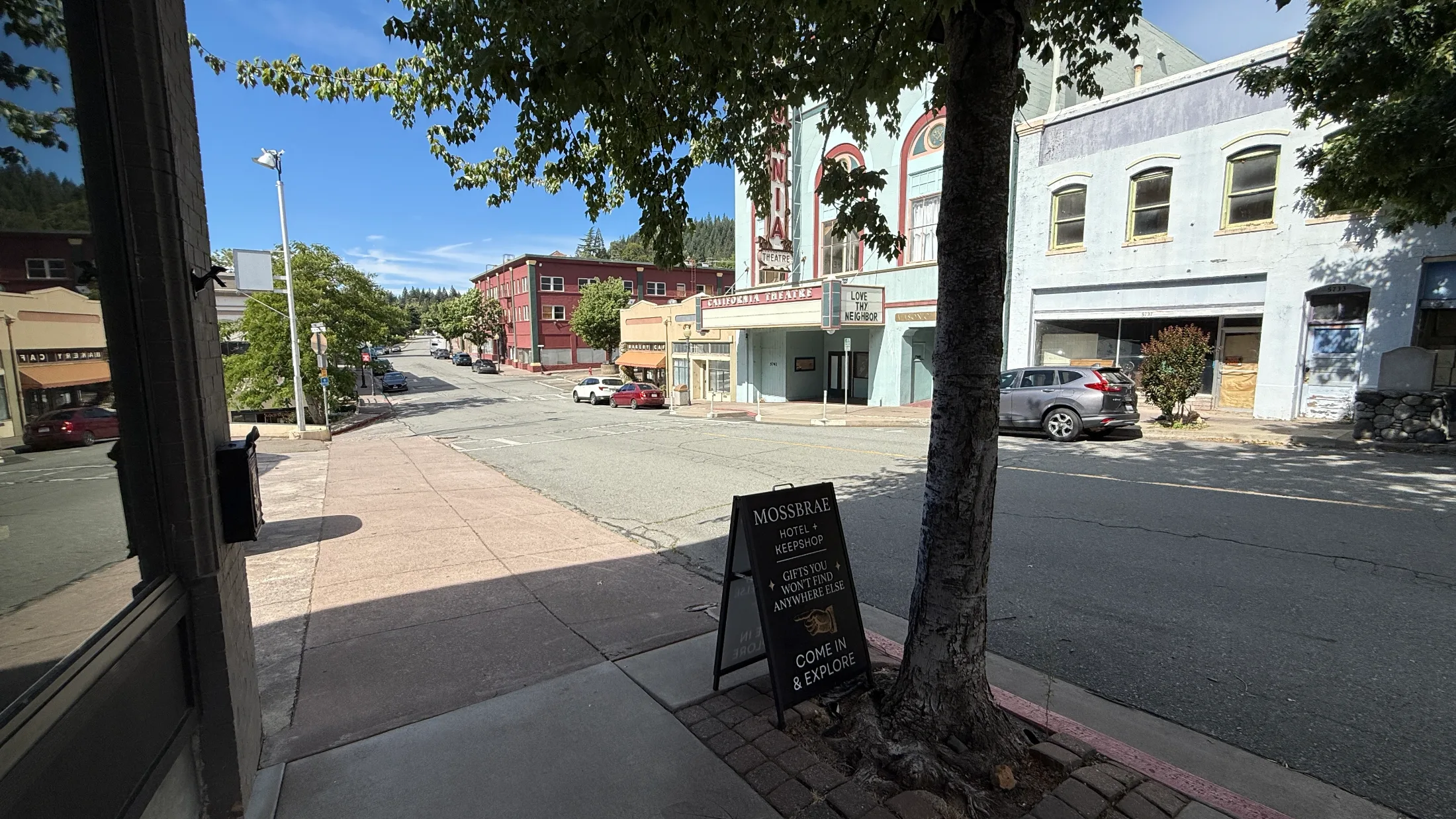 A-frame sidewalk sign for Mossbrae Hotel and Keepshop on Dunsmuir Avenue with the California Theatre visible across the street