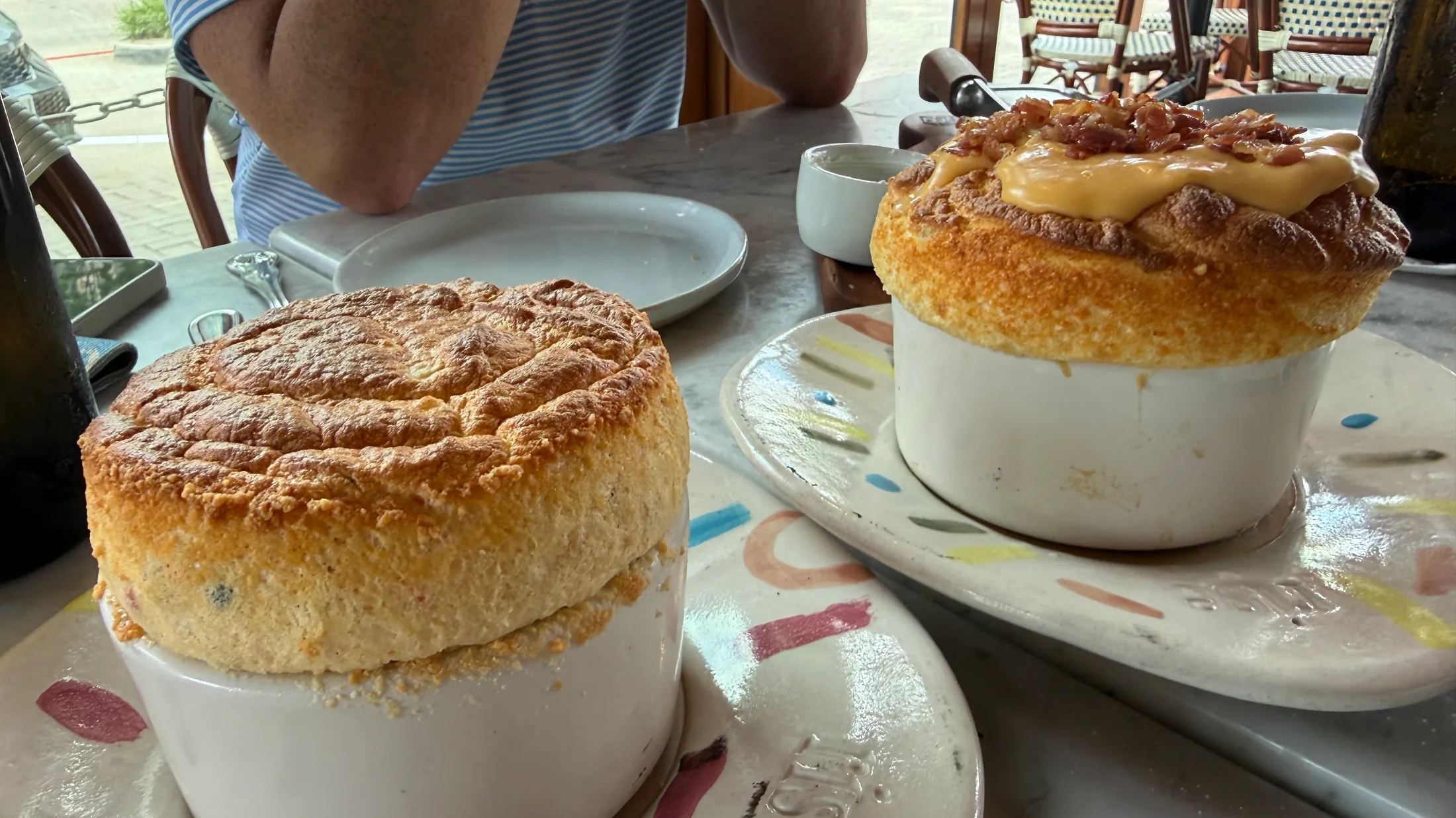 Two savory soufflés side by side on the table at Rise Soufflé Fort Worth, one golden and one topped with cheese sauce and bacon