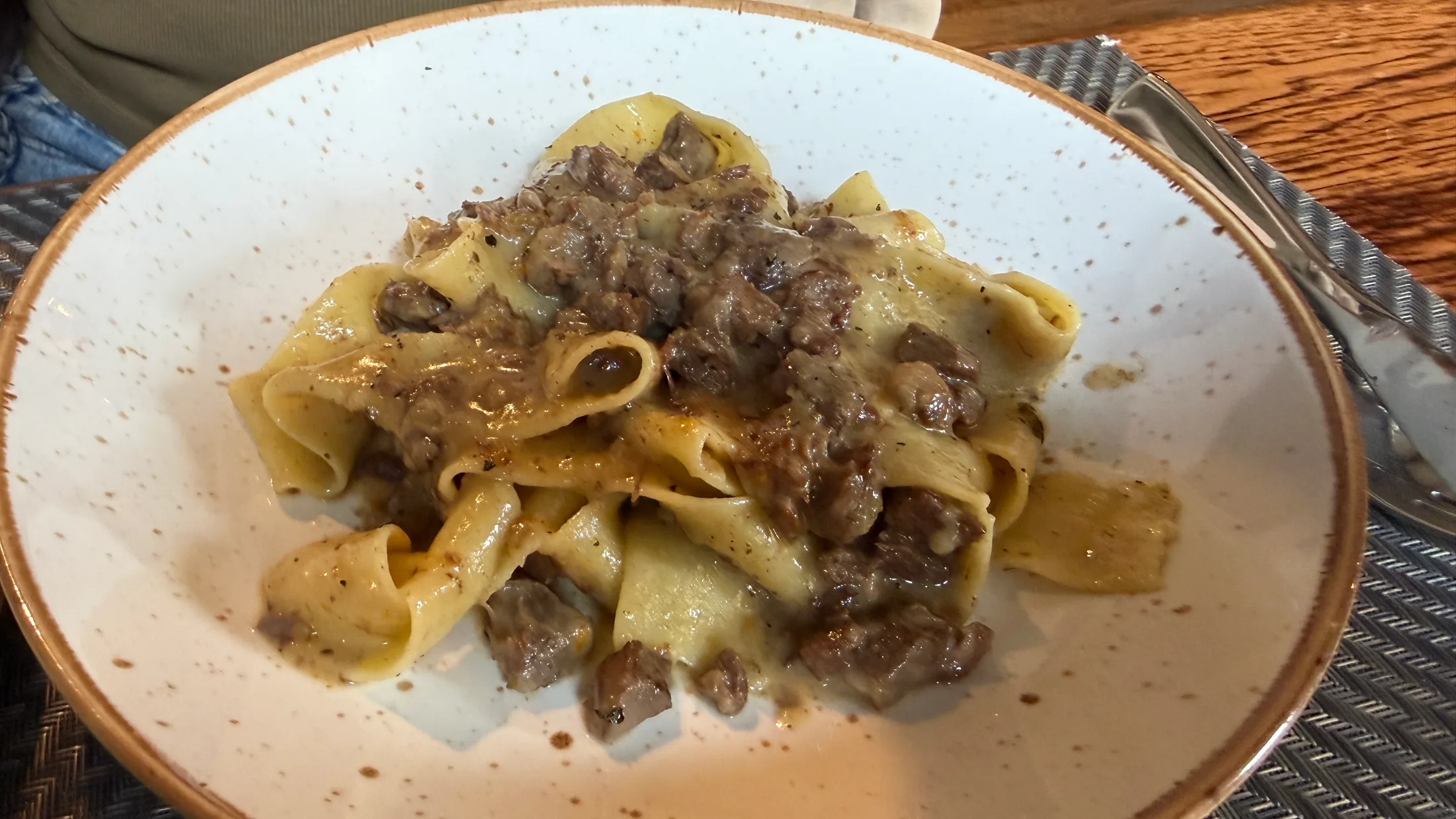 A bowl of house-made pappardelle with lamb ragù and crushed pistachios, the wide ribbons of pasta coated in a deep, glossy sauce
