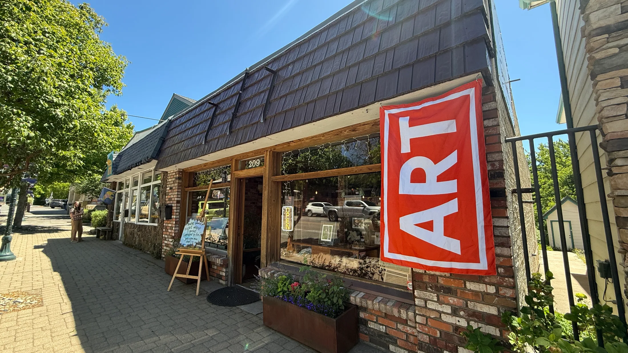 Exterior of Redwood Gallery at 209 N. Mt. Shasta Blvd. on a sunny day, with a large red ART banner hanging by the door