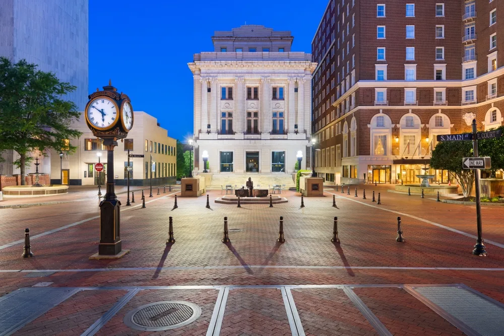 Greenville South Carolina civic square at dusk — brick pavers, an ornate street clock, a lit neoclassical building, quiet streets