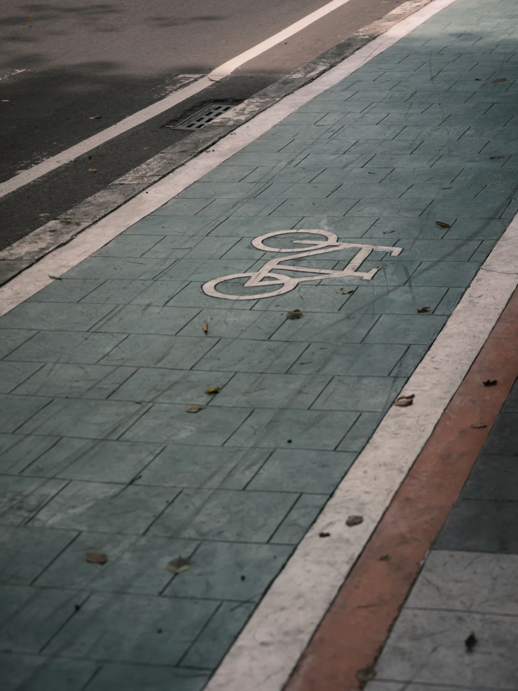 Close-up of a teal protected bike lane with a white bicycle symbol painted on paving stones, separated from traffic by a white stripe