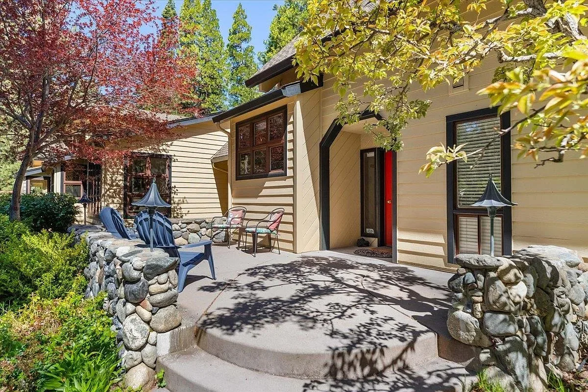 Front patio of 1405 Audubon Rd with river-rock wall, Adirondack chairs, Japanese maple, and red front door