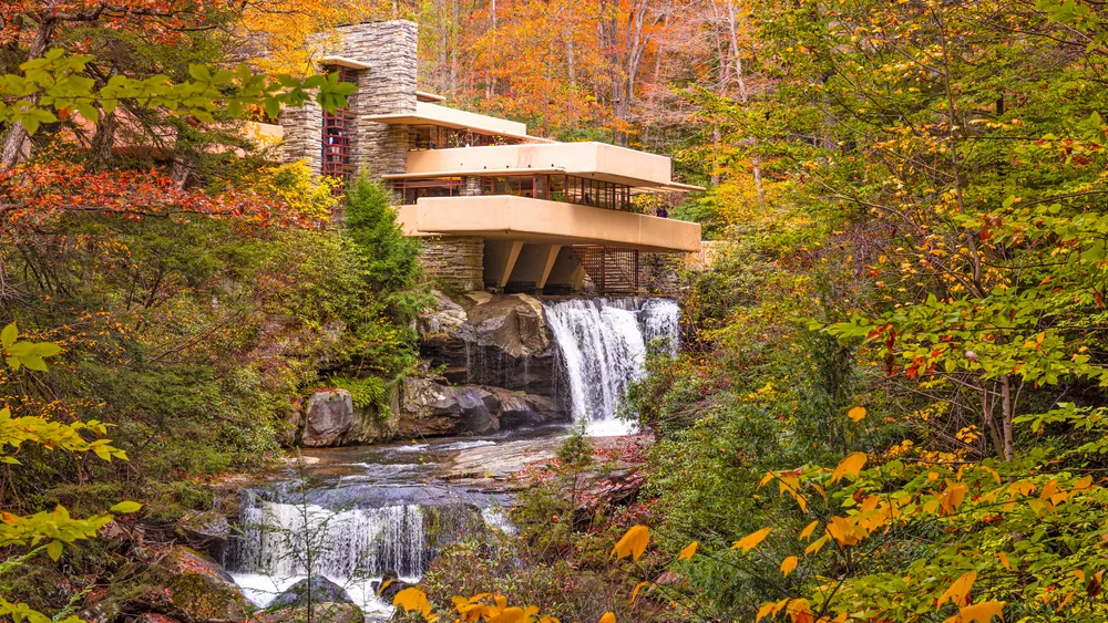 A cantilevered stone and concrete structure built directly over a waterfall surrounded by dense autumn foliage