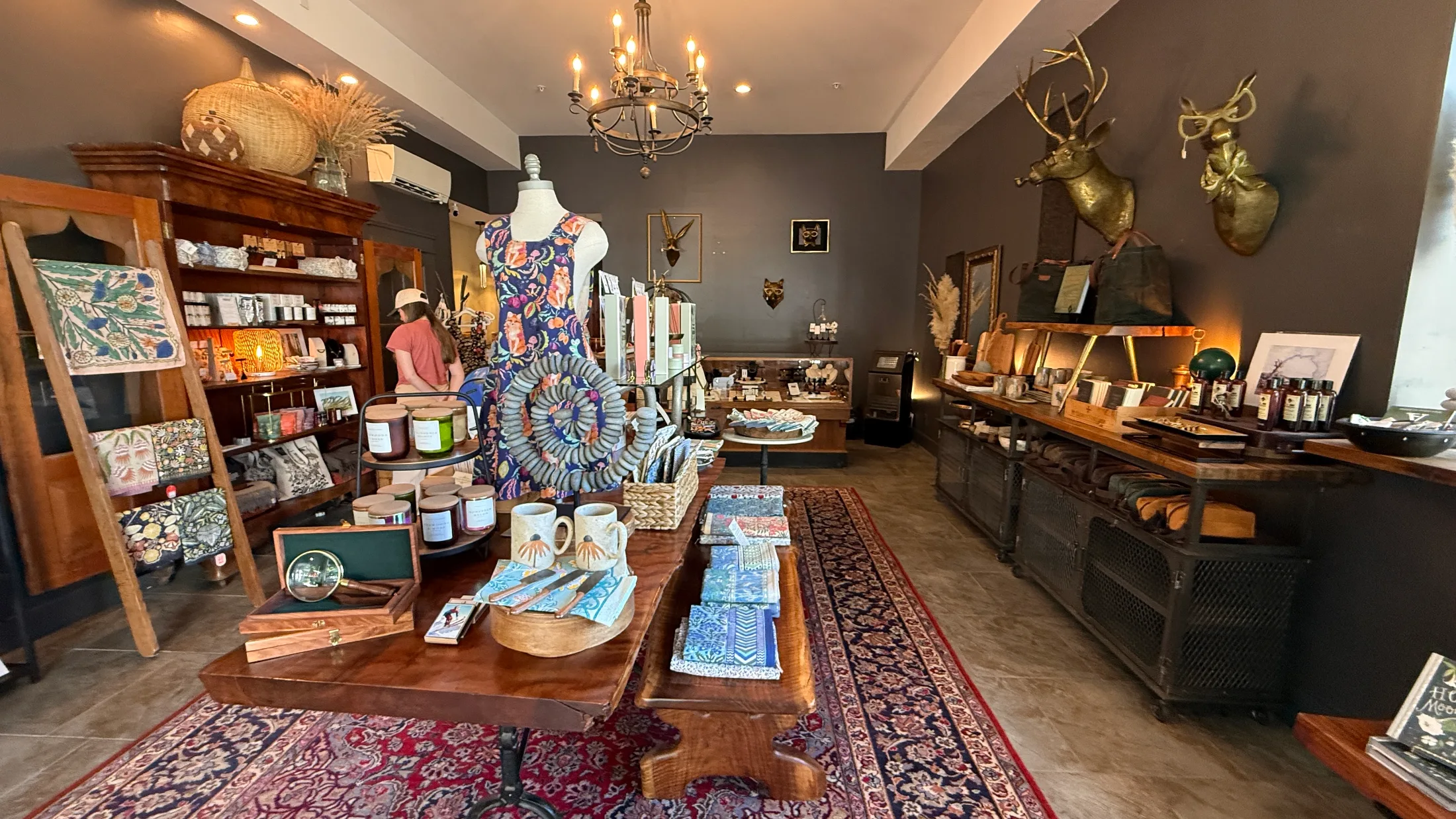 Wide interior view of the Mossbrae Keepshop showing the full room with chandelier, brass stag and fox mounts, and curated merchandise