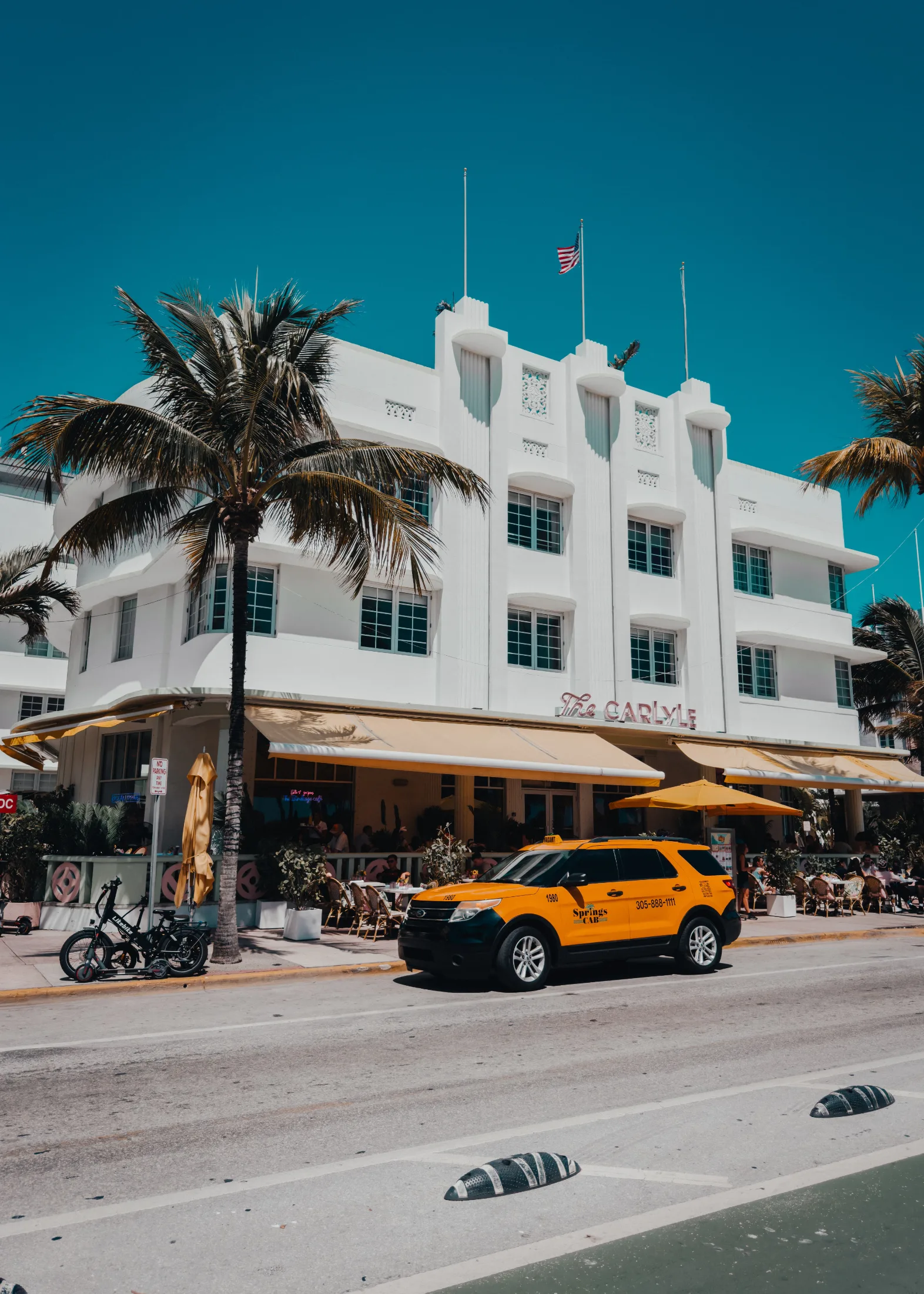 The Carlyle Hotel on Ocean Drive, Miami Beach, with a yellow taxi parked out front under a brilliant blue sky