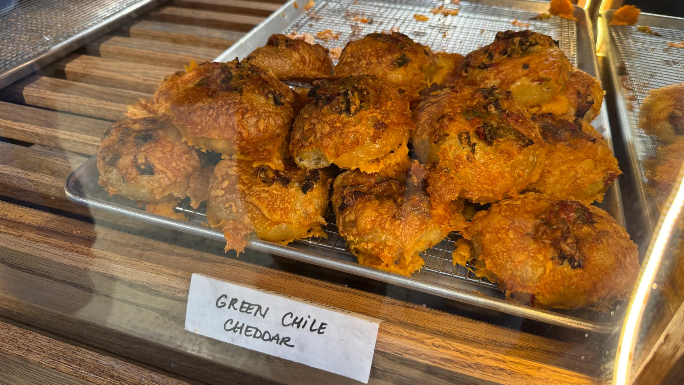 Tray of green chile cheddar bagels in the display case at Sunday Bagels, crusted orange with charred chile flecks