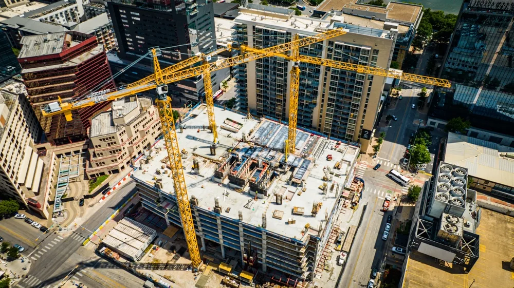 Aerial view of an active urban construction site with three yellow tower cranes, fresh concrete, and surrounding city blocks