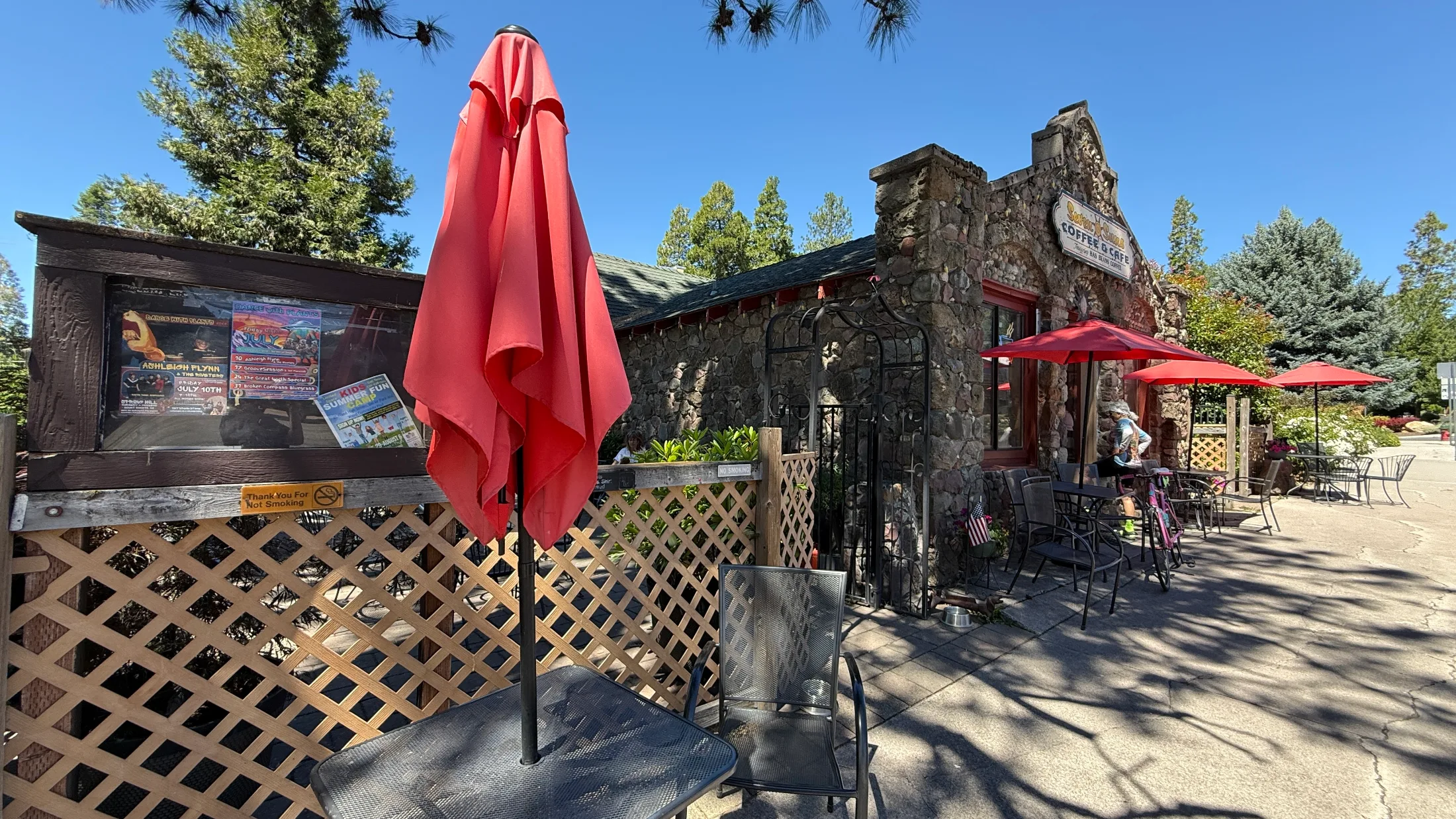 Seven Suns Coffee & Café stone building from the patio side, with red umbrellas and morning light filtering through the pines