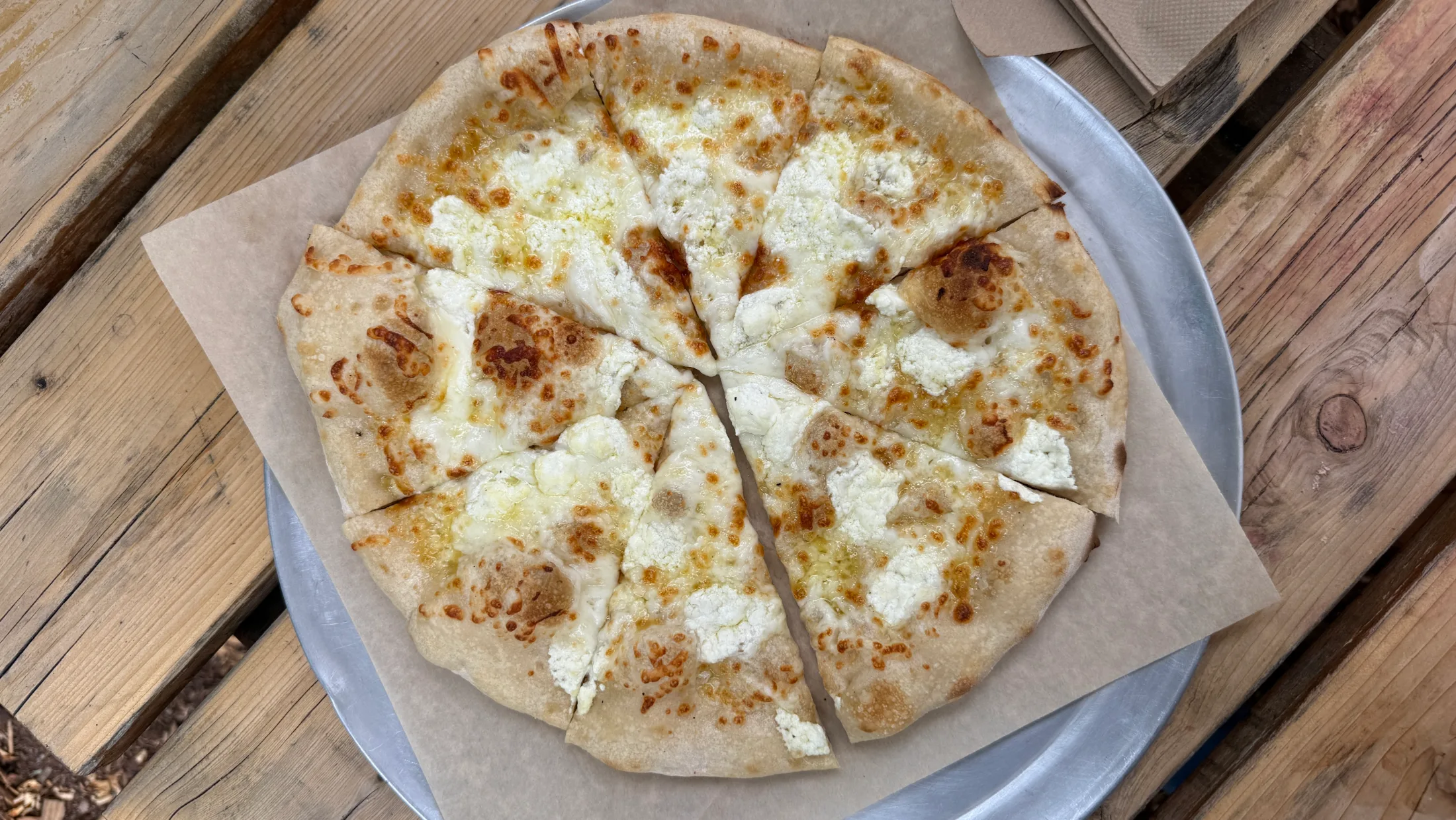 Wood-fired white pizza with ricotta and melted mozzarella, sliced on a metal pan over parchment paper
