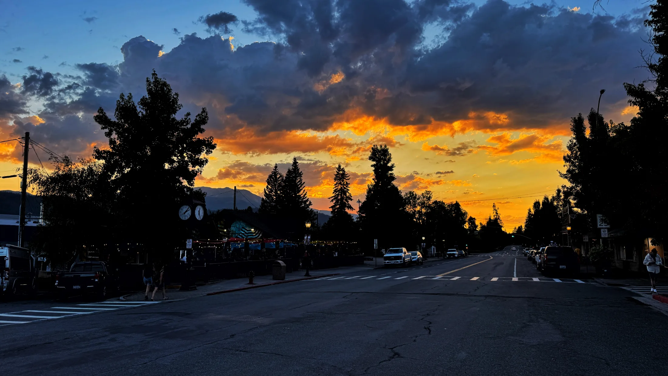 Mount Shasta boulevard at sunset, string lights glowing outside a downtown restaurant as an orange and violet sky burns above the treeline