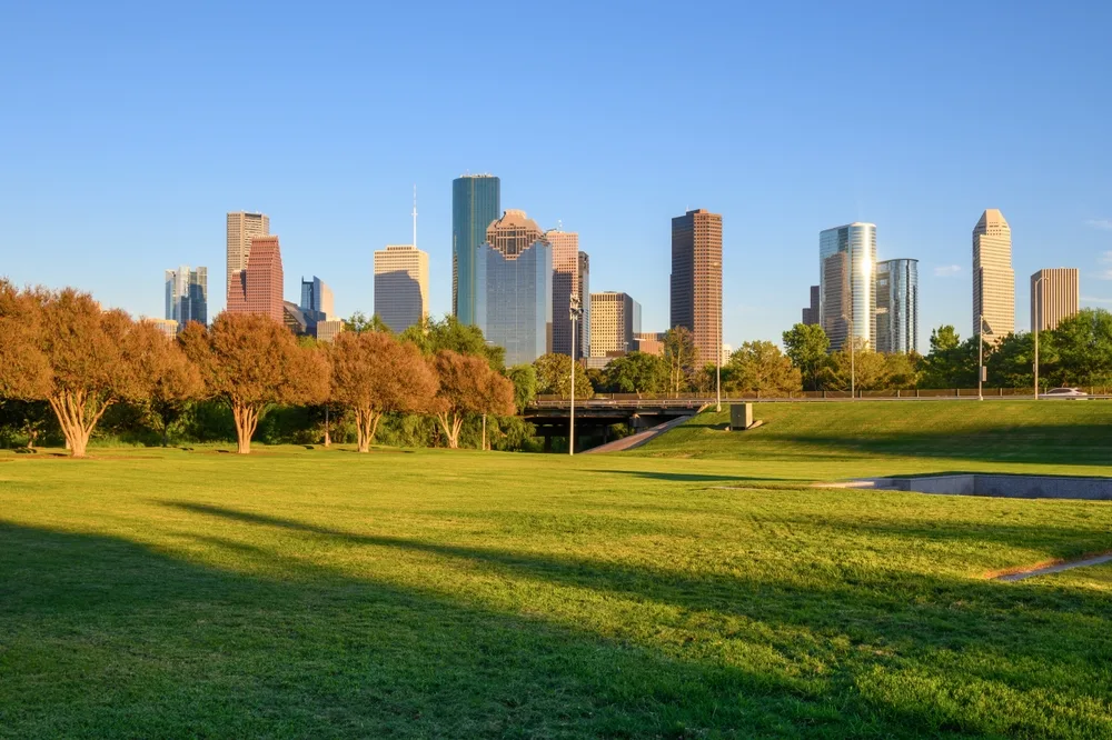 Houston skyline at golden hour seen across a wide green park, towers glowing warm in afternoon light