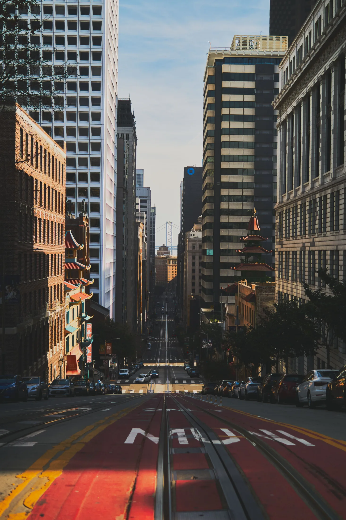 Early morning on a San Francisco street with cable car tracks, Chinatown architecture on the left, the Bay Bridge in the distance