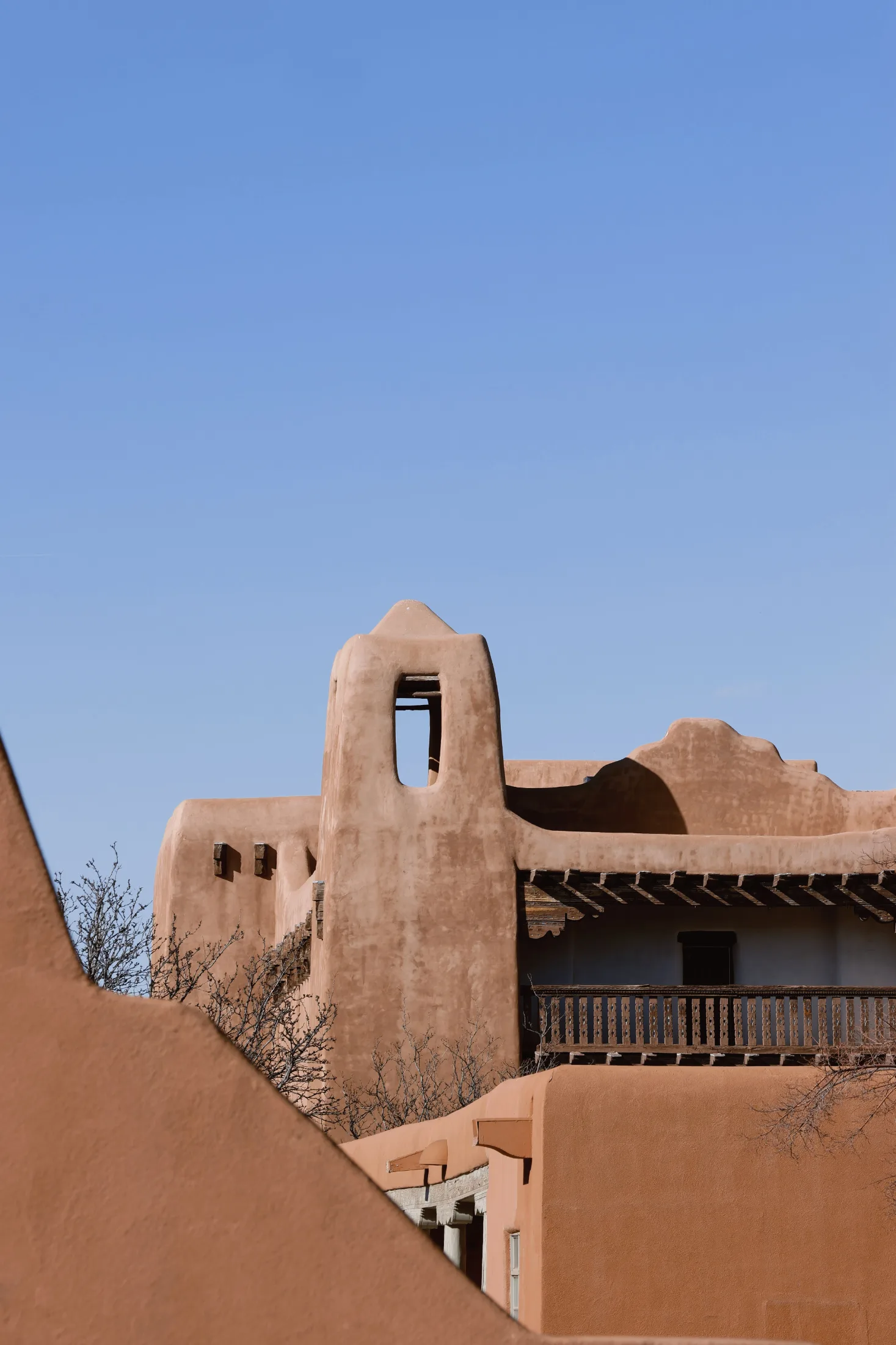 Stacked adobe rooflines and a bell tower rising against clear blue sky in downtown Santa Fe